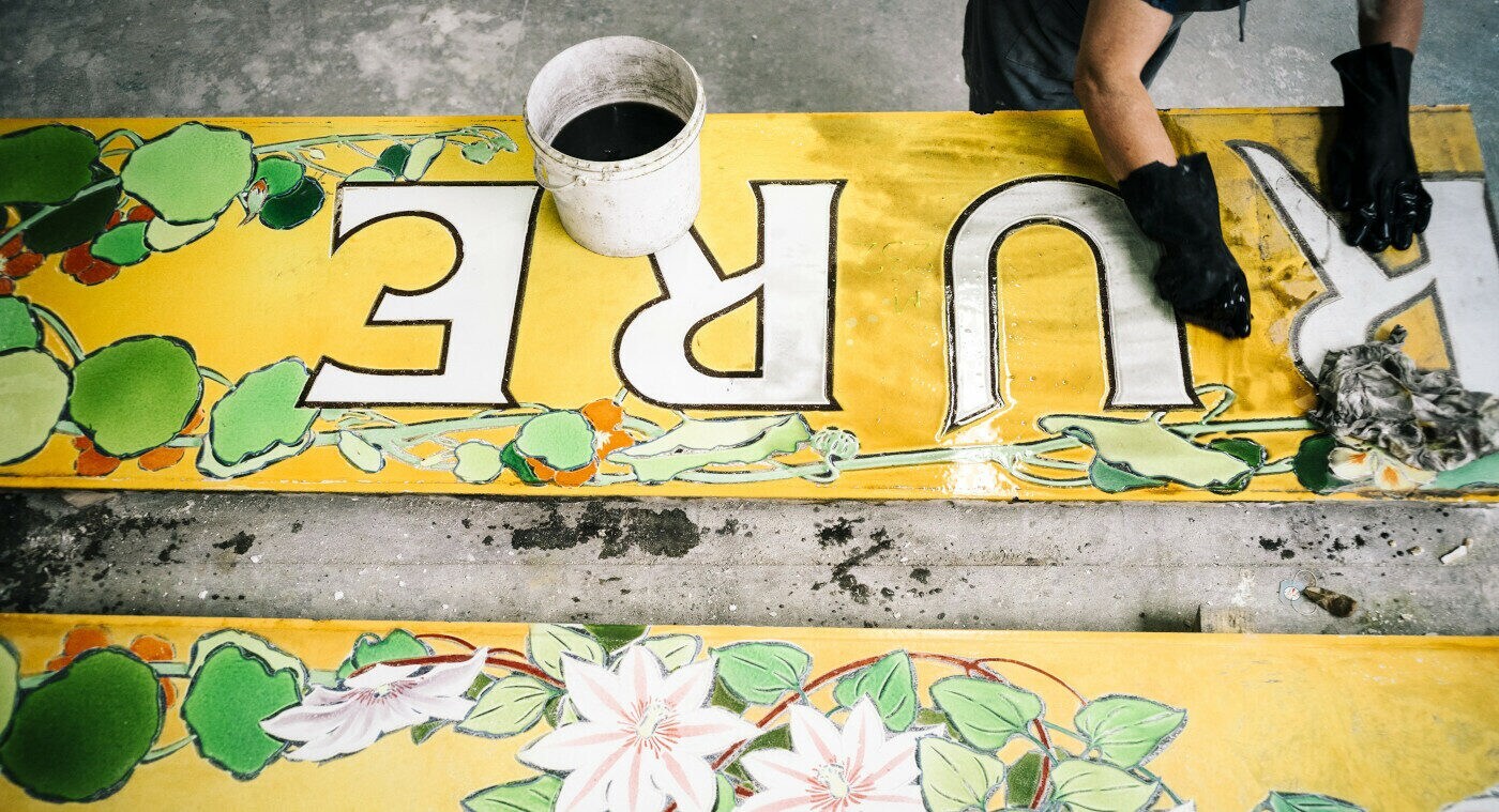 Ein großes, altes Emaille-Schild wird von Hand restauriert