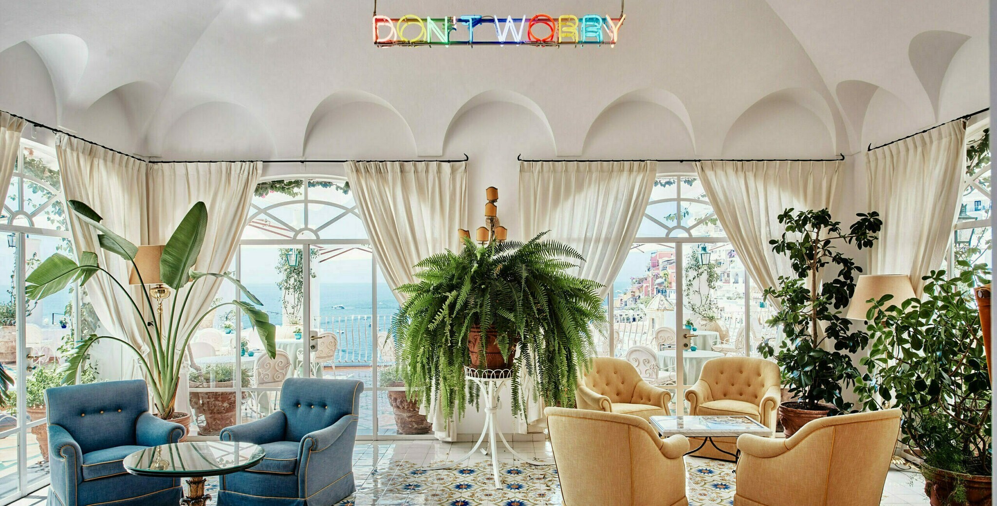 Eine helle Bar mit Panoramafenstern, gemütlichen Sesseln und einer Neonlicht-Installation mit dem Schriftzug “Don’t Worry”