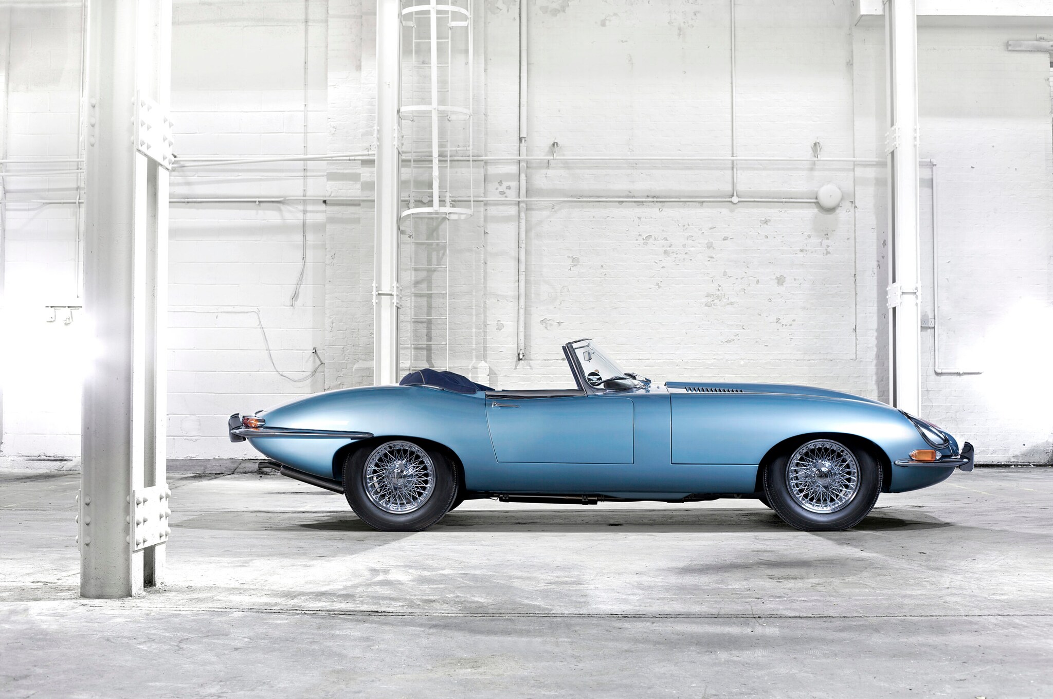 Ein blauer E-Type Roadster von der Seite in einem Industriebau