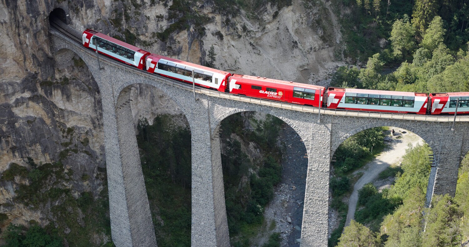 Vogelperspektive eines roten Zuges, der auf einem Viadukt durch eine Berglandschaft fährt Vogelperspektive eines roten Zuges, der auf einem Viadukt durch eine Berglandschaft fährt