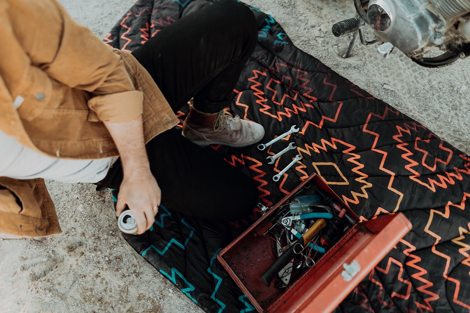 Ein Mann kniet neben Werkzeugkiste auf Decke am Boden