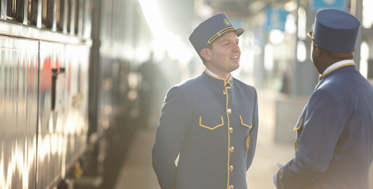 Ein Zug steht im Bahnhof, daneben zwei männliche Zugbegleiter in blauen Uniformen auf dem Bahnsteig Ein Zug steht im Bahnhof, daneben zwei männliche Zugbegleiter in blauen Uniformen auf dem Bahnsteig