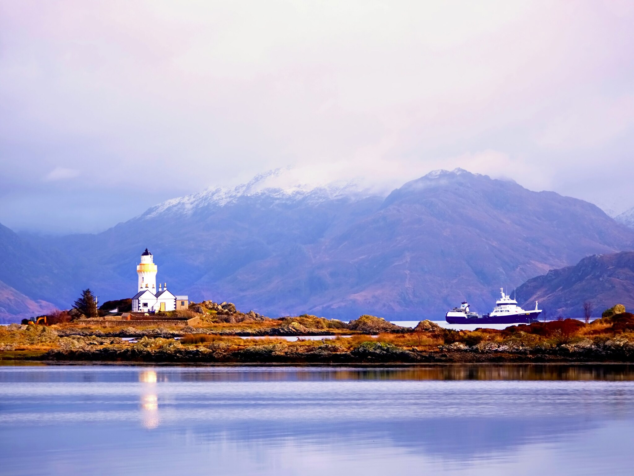 Ein weißer Leuchtturm nahe der Isle of Skye vor Bergpanorama
