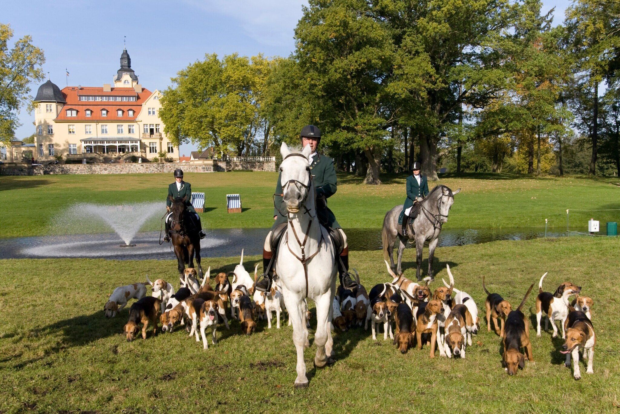 Drei Reiter auf Pferden umgeben von Jagdhunden im Schlossgarten