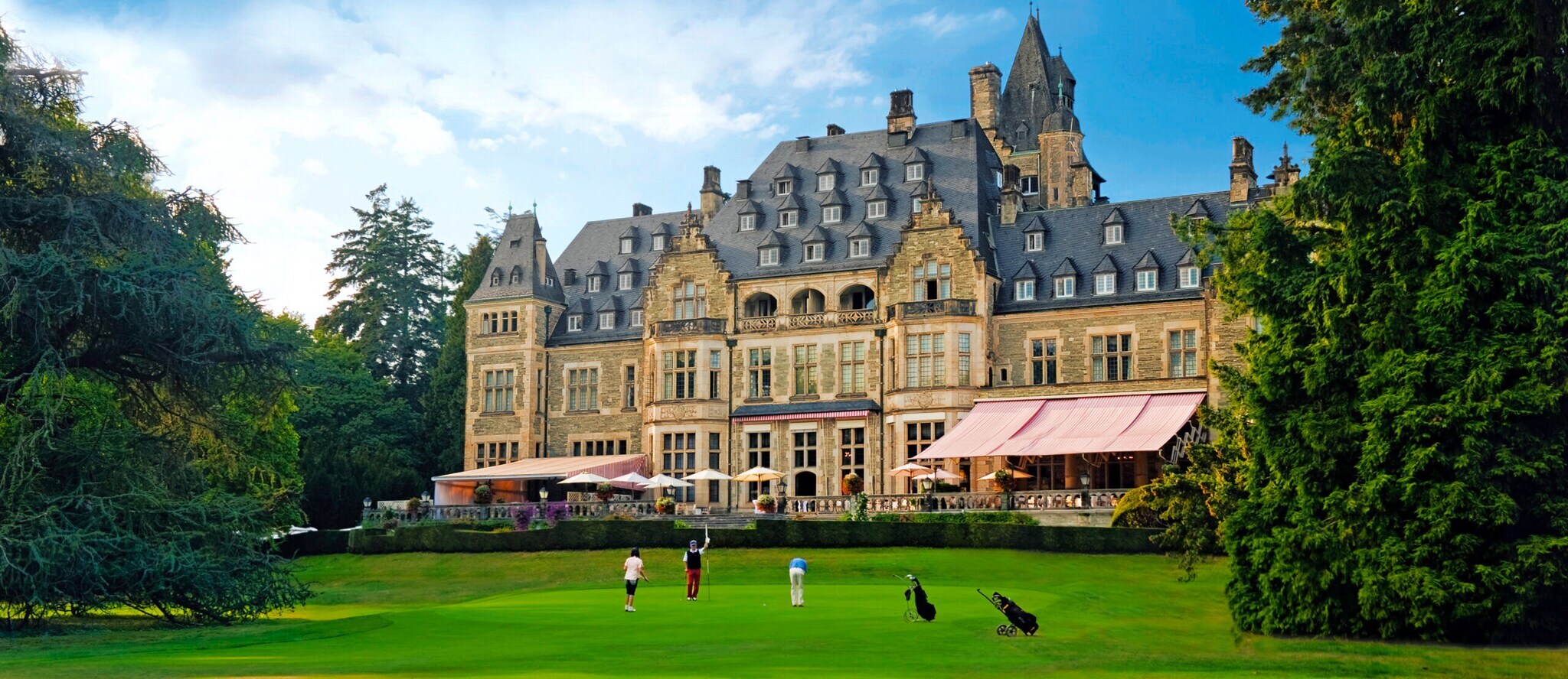 Außenaufnahme von Schlosshotel mit Terrasse, davor Rasen mit Golfenden