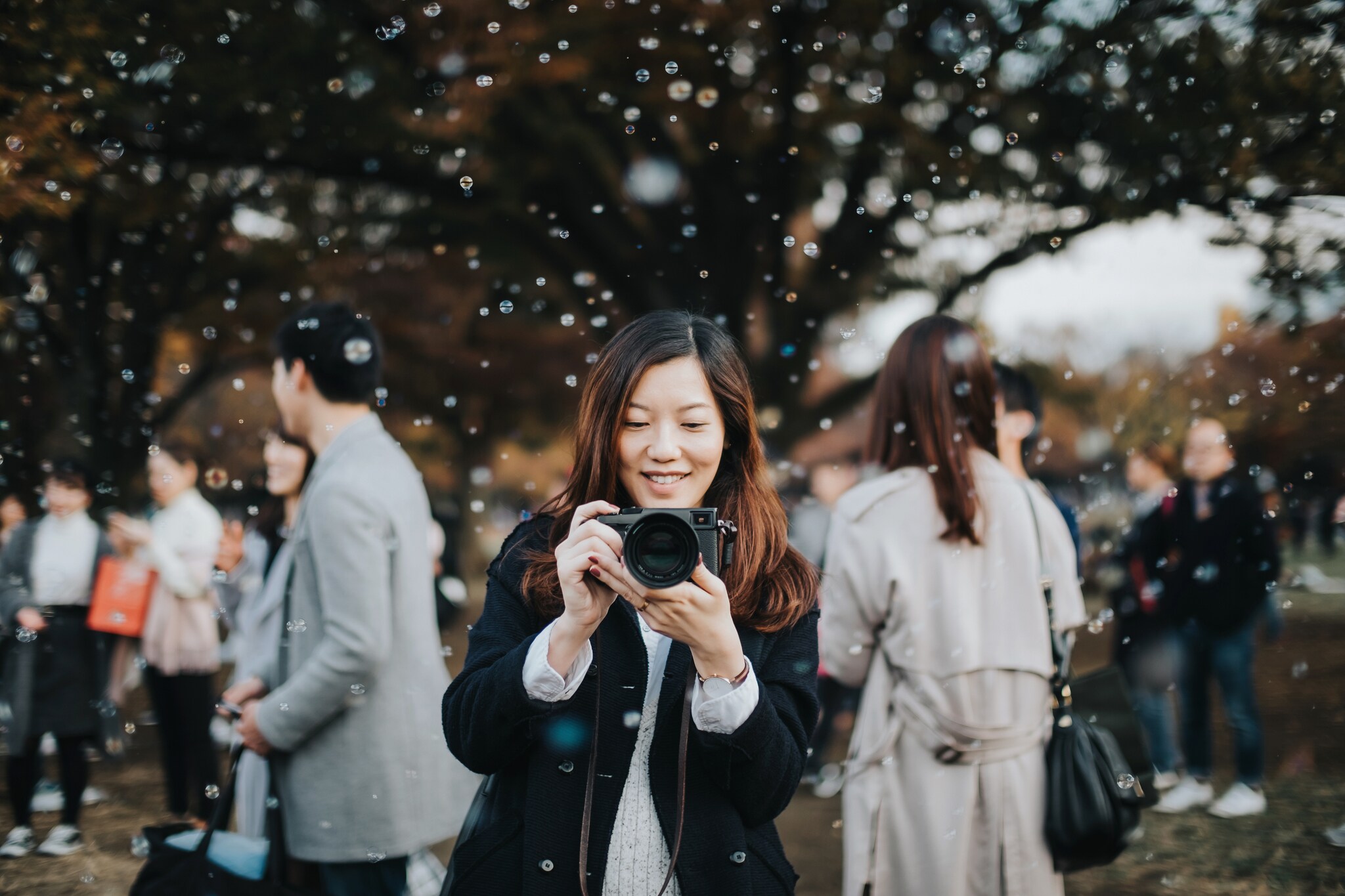 Eine Frau mit Kamera in der Hand steht inmitten einer Wolke aus Seifenblasen