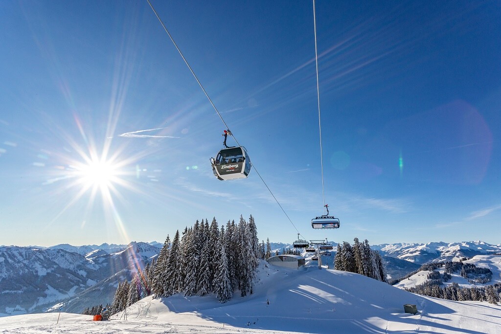 Zwei Menschen von hinten in einem Liegestuhl, sie blicken auf die verschneiten Berge des Skigebiets Wilder Kaiser