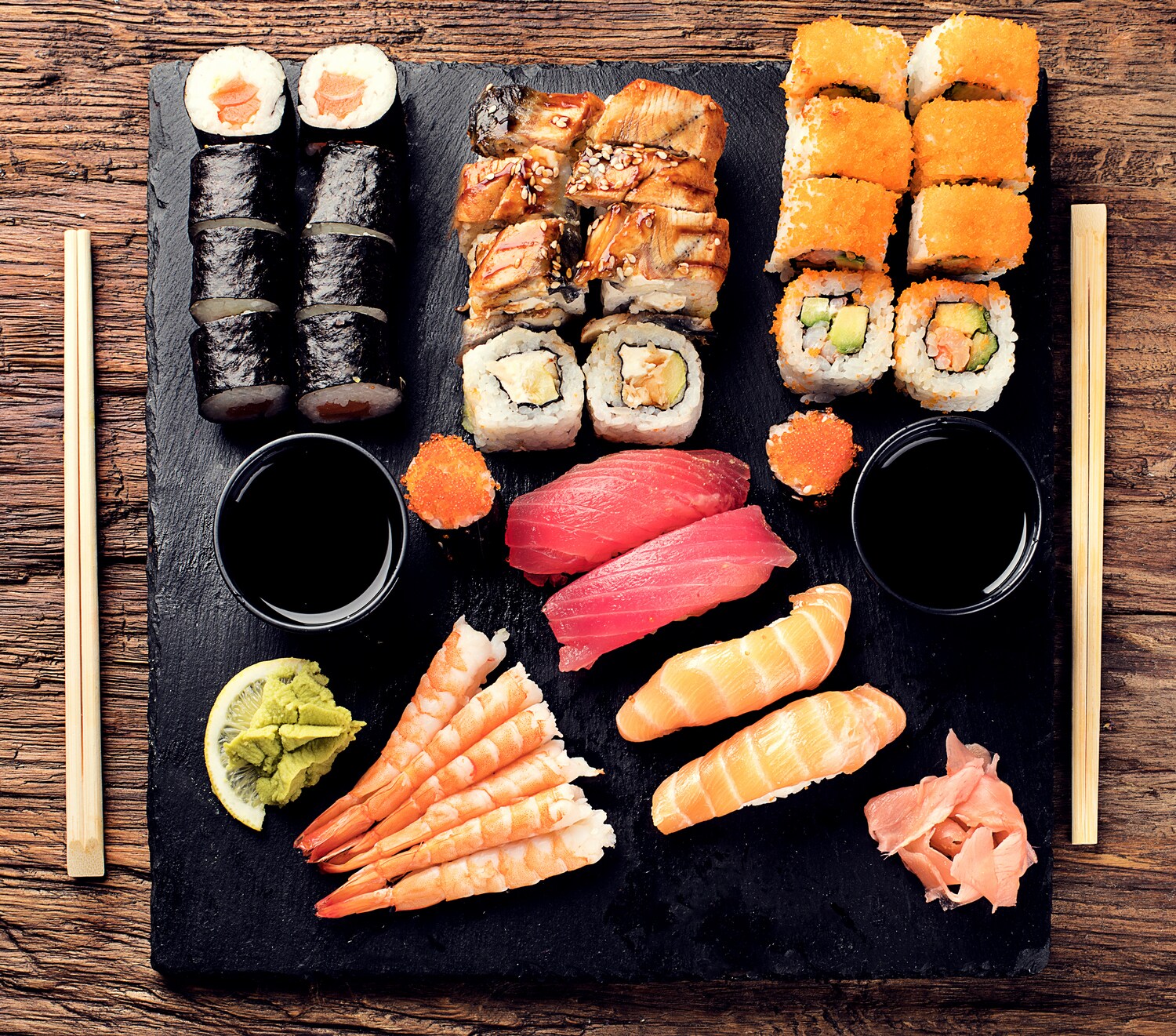 Aufsicht unterschiedlicher Sushi-Sorten mit Beilagen auf schwarzem Tablett Aufsicht unterschiedlicher Sushi-Sorten mit Beilagen auf schwarzem Tablett