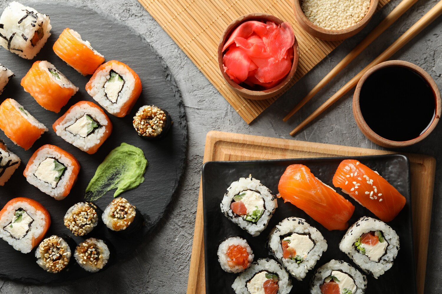 Aufsicht unterschiedlicher Sushi-Sorten auf zwei Tellern, daneben Beilagen und Stäbchen Aufsicht unterschiedlicher Sushi-Sorten auf zwei Tellern, daneben Beilagen und Stäbchen