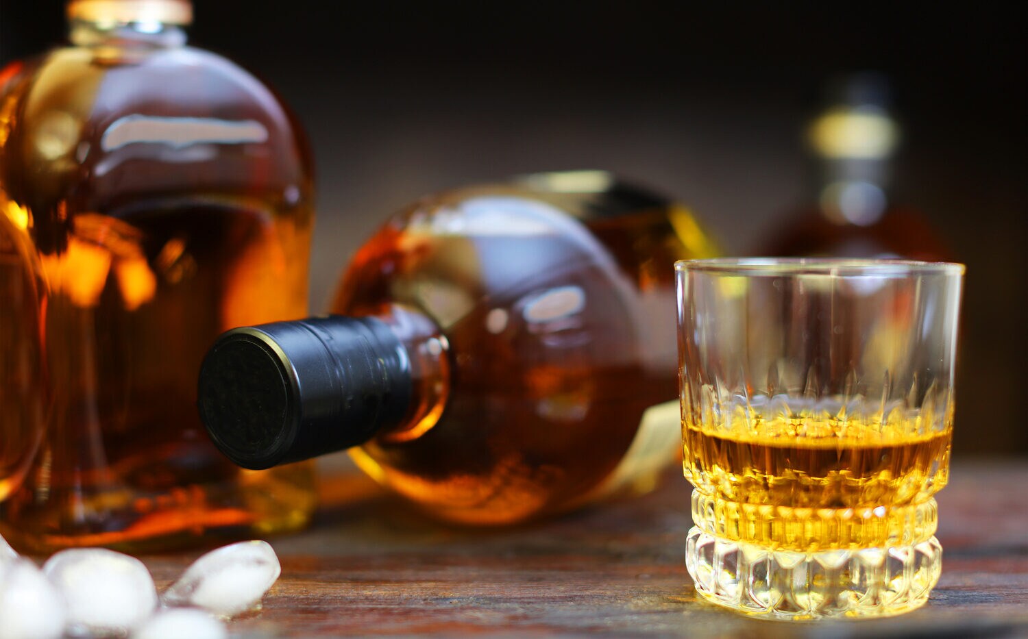 Ein Glas mit Whisky vor einer stehenden und einer liegenden Flasche auf einem Tisch