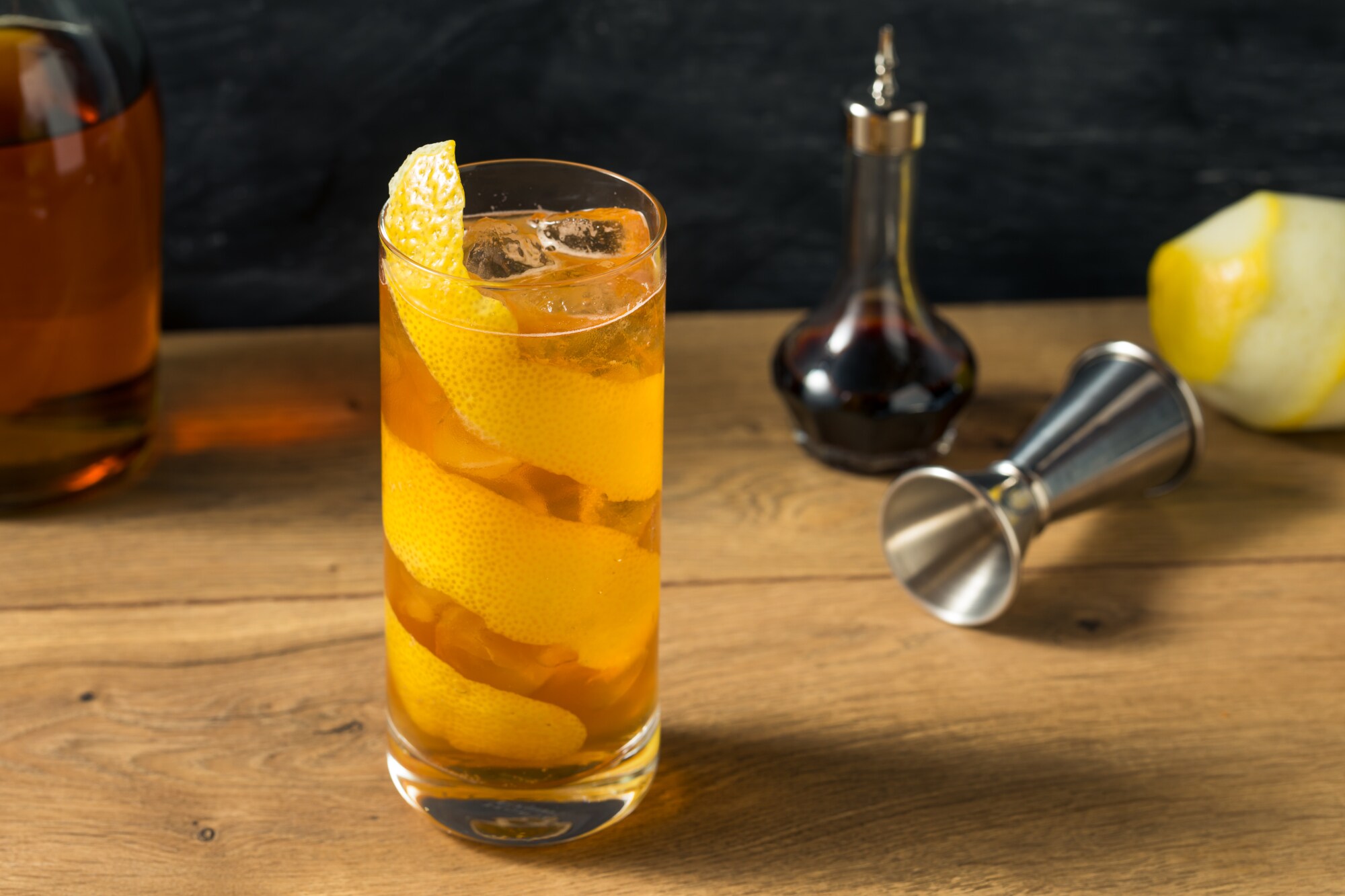 Cocktail mit Zitronenschale auf Holztisch, daneben Zutaten und Messbecher