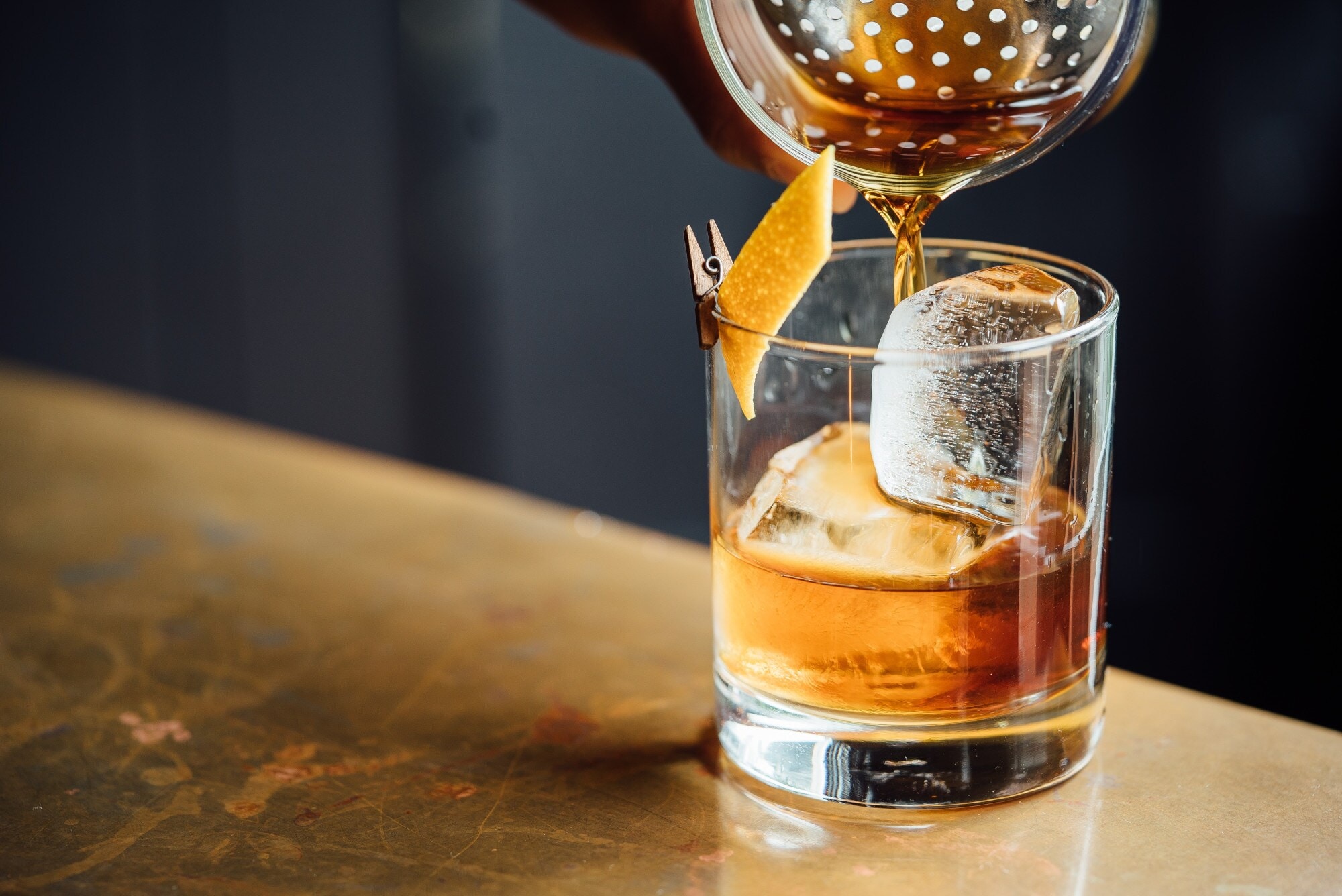 Ein Trinkglas mit Eis und Zitronenschale wird mit Whisky befüllt Ein Trinkglas mit Eis und Zitronenschale wird mit Whisky befüllt