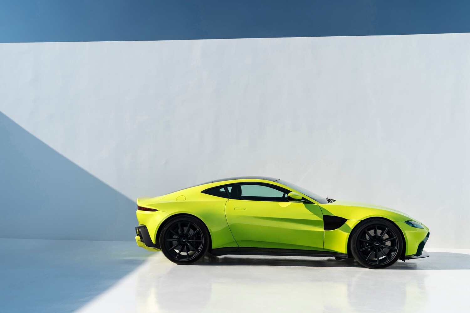 Ein Aston Martin Vantage in gelb-grüner Autofarbe Lime Essence vor einer weißen Wand