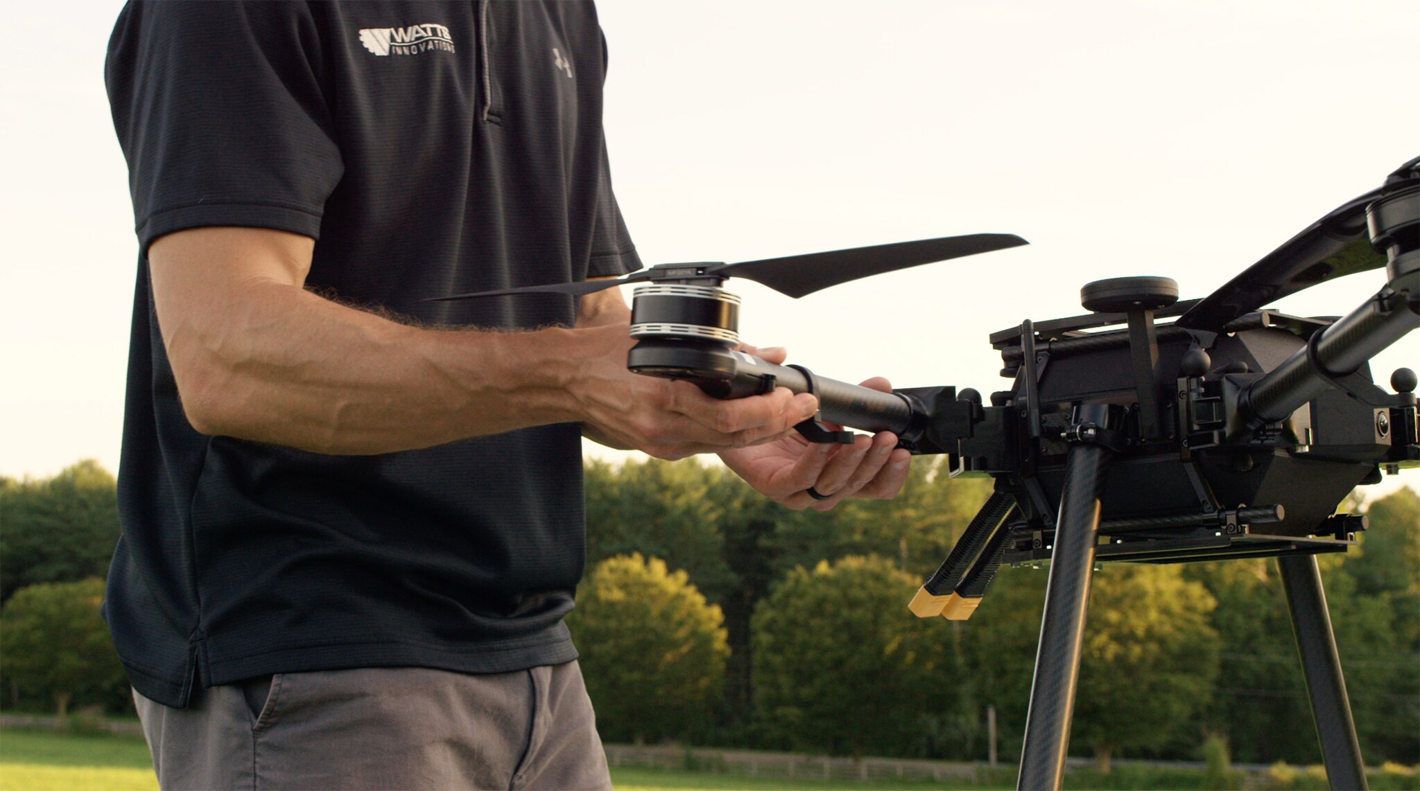 Ein Mann steht neben einer schwarzen Drohne und justiert einen Arm