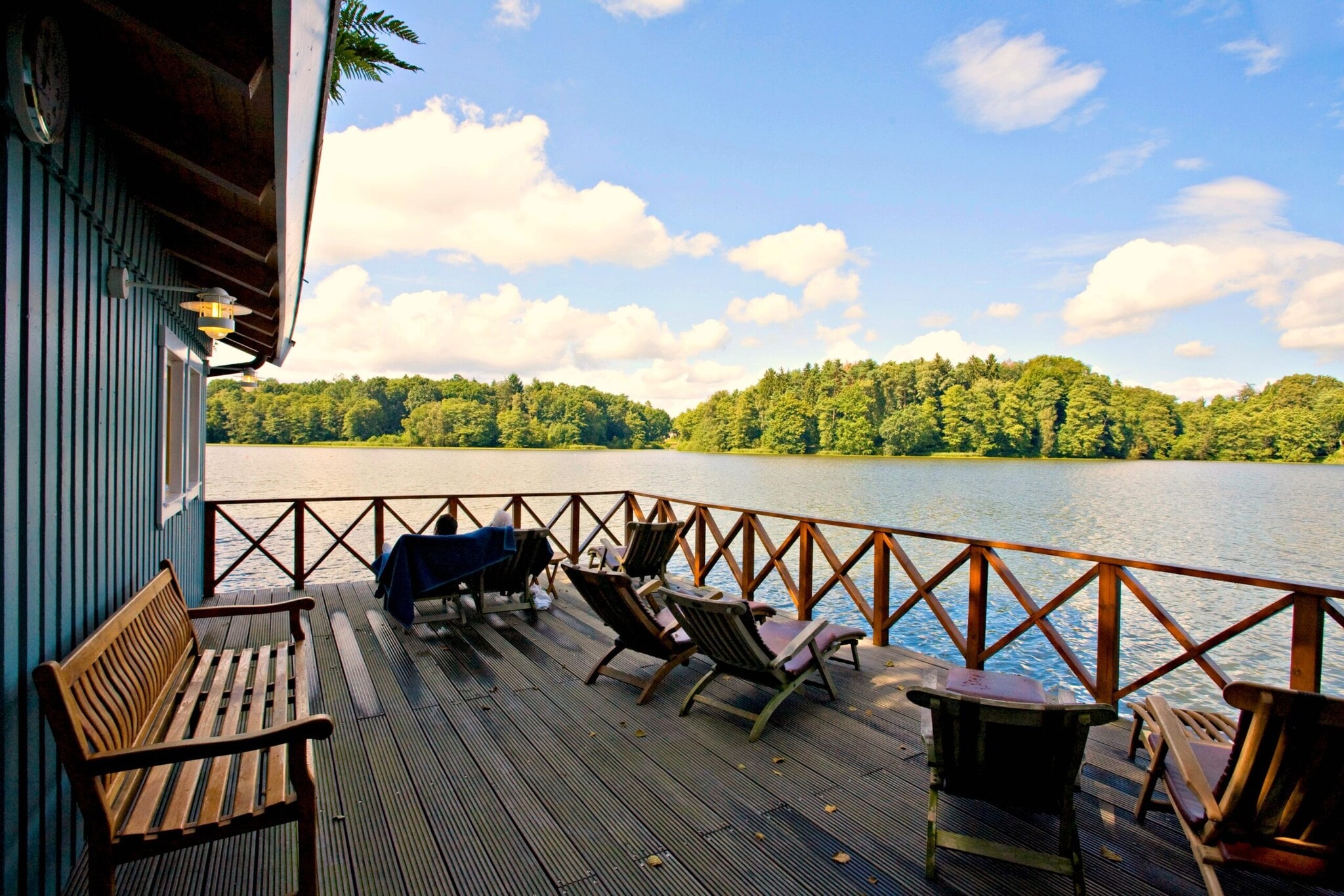 Eine Terrasse mit Liegestühlen an einem Holzhaus am Ufer eines Sees Eine Terrasse mit Liegestühlen an einem Holzhaus am Ufer eines Sees