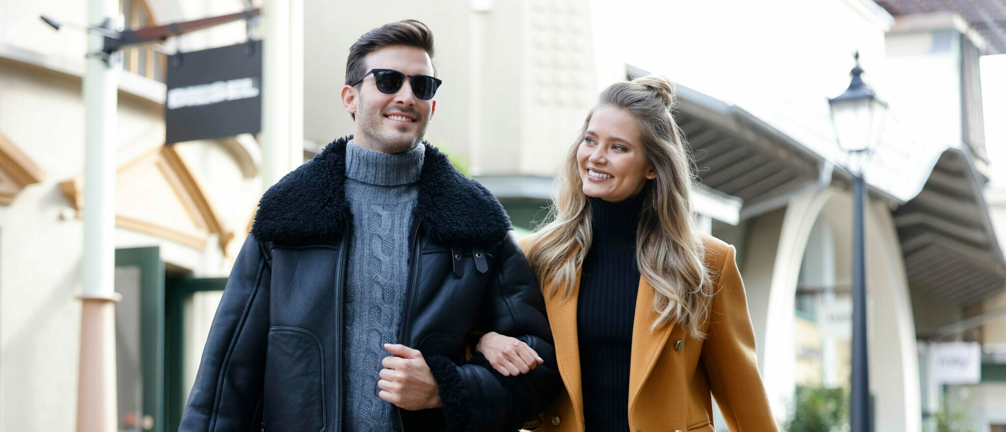 Ein junges, lachendes Paar geht Arm in Arm durch eine Einkaufsstraße