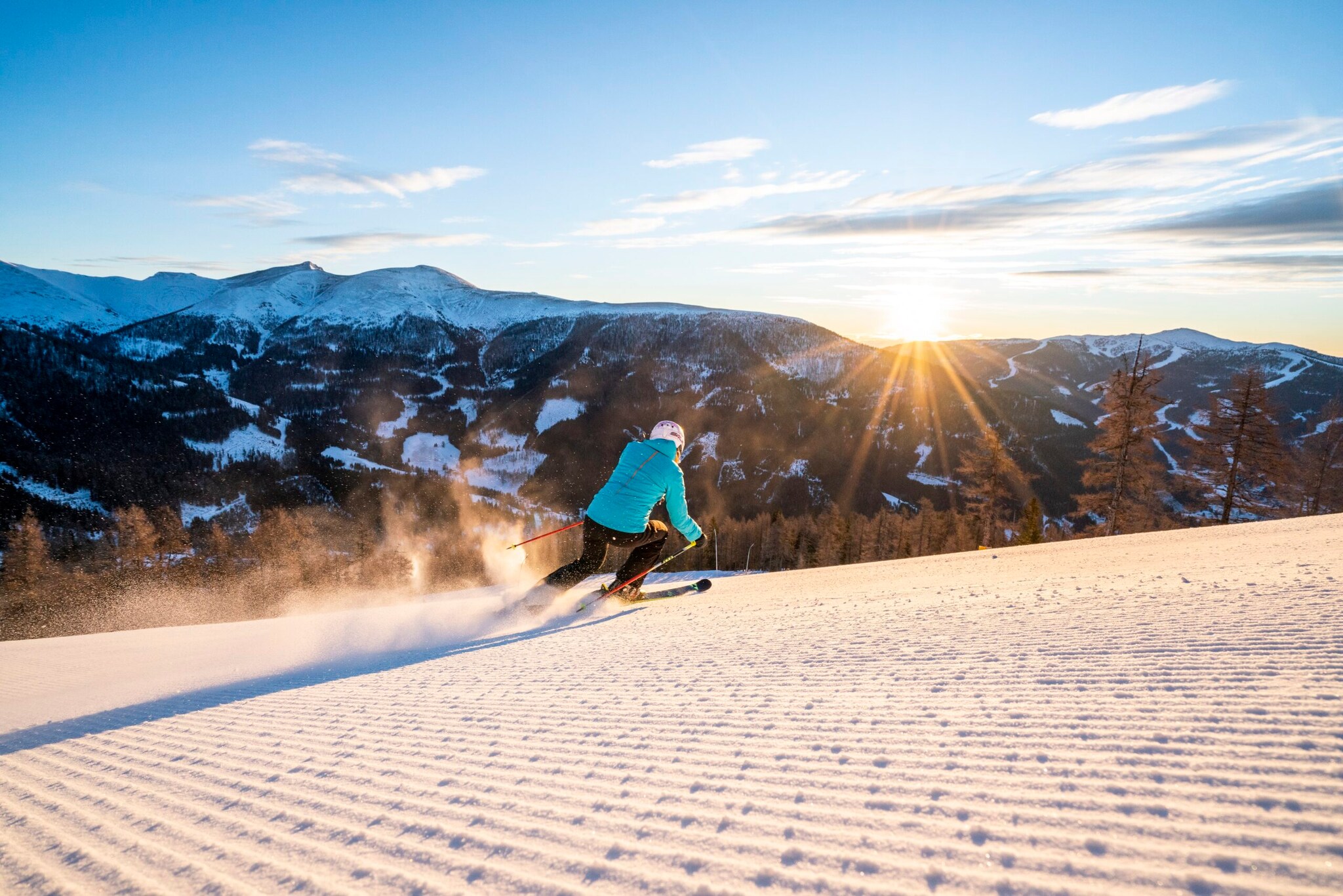 Eine Person auf Ski fährt bei Sonnenschein eine Piste hinab.