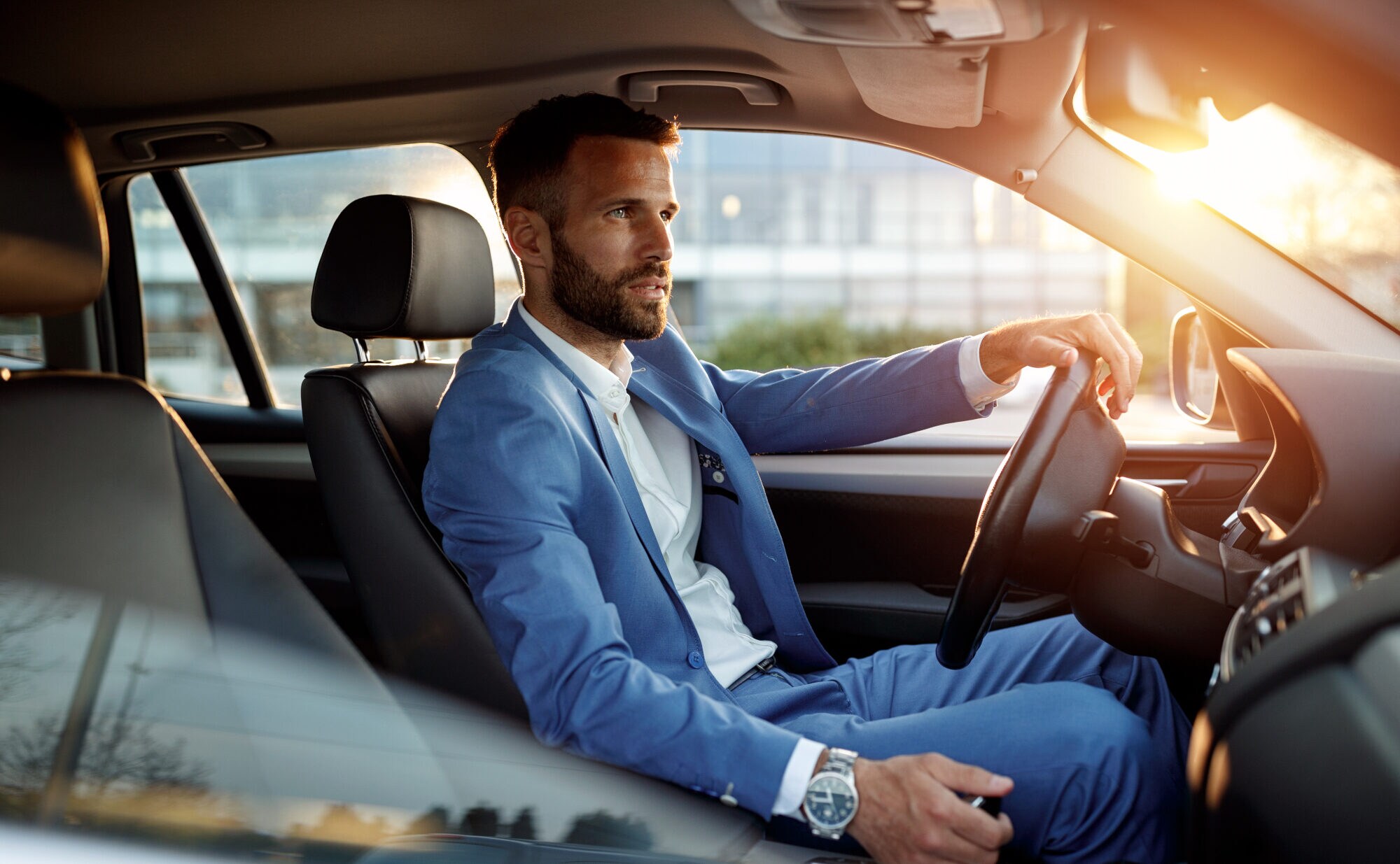 Ein Mann im Anzug sitzt in einem Auto, im Hintergrund Sonnenschein Ein Mann im Anzug sitzt in einem Auto, im Hintergrund Sonnenschein