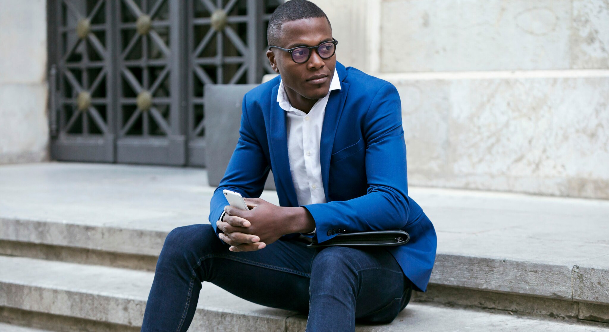 Ein Mann in Jeans und blauem Sakko sitzt auf einer Treppe.