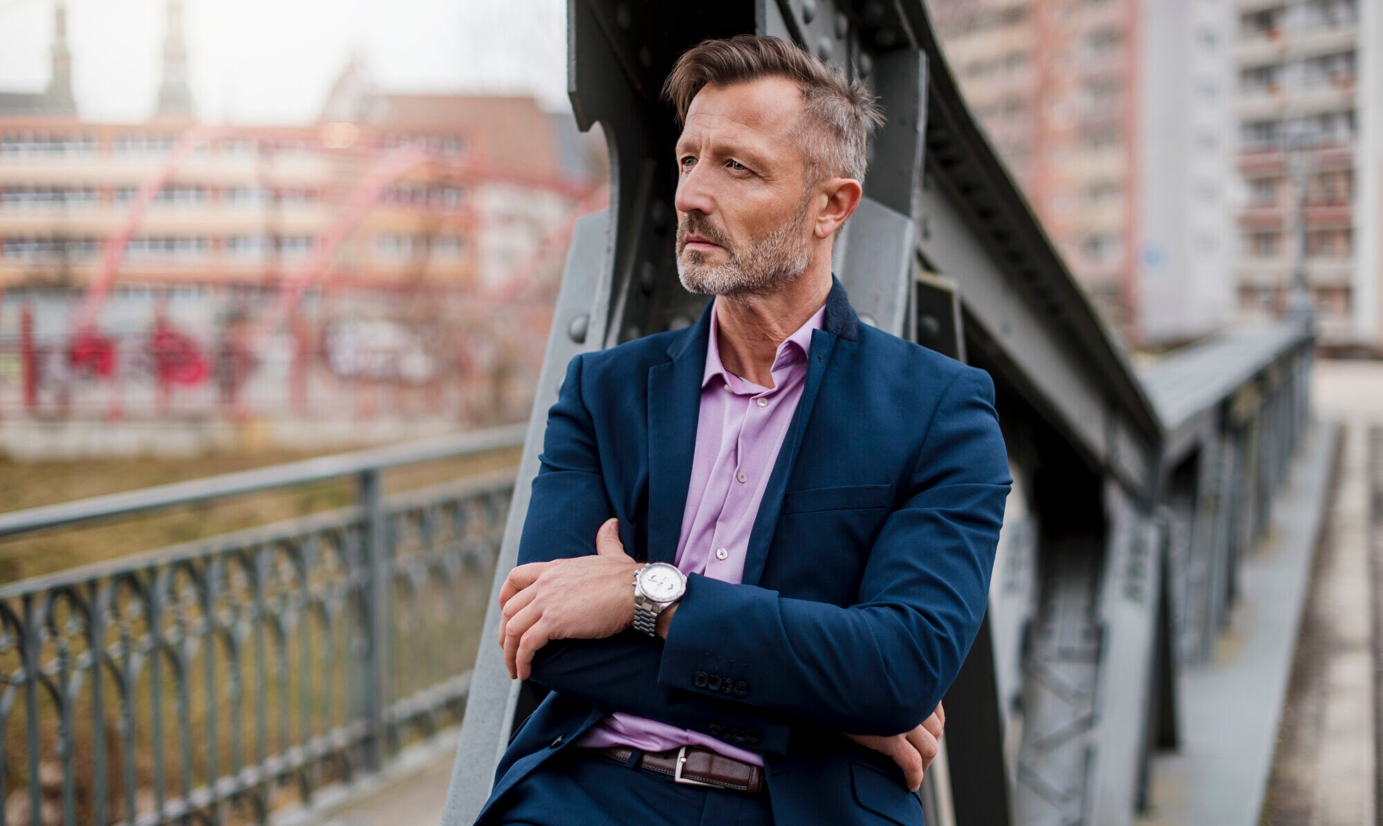Ein Mann in Anzug und Hemd sitzt auf einem Brückengeländer