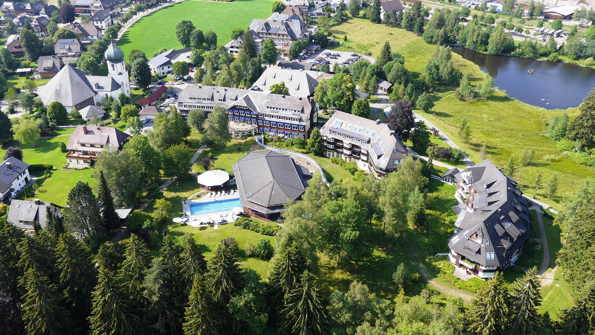 Herrschaftliches Anwesen und Hotelkomplex mit Swimmingpool in begrünter Umgebung mit Wald und See aus der Vogelperspektive