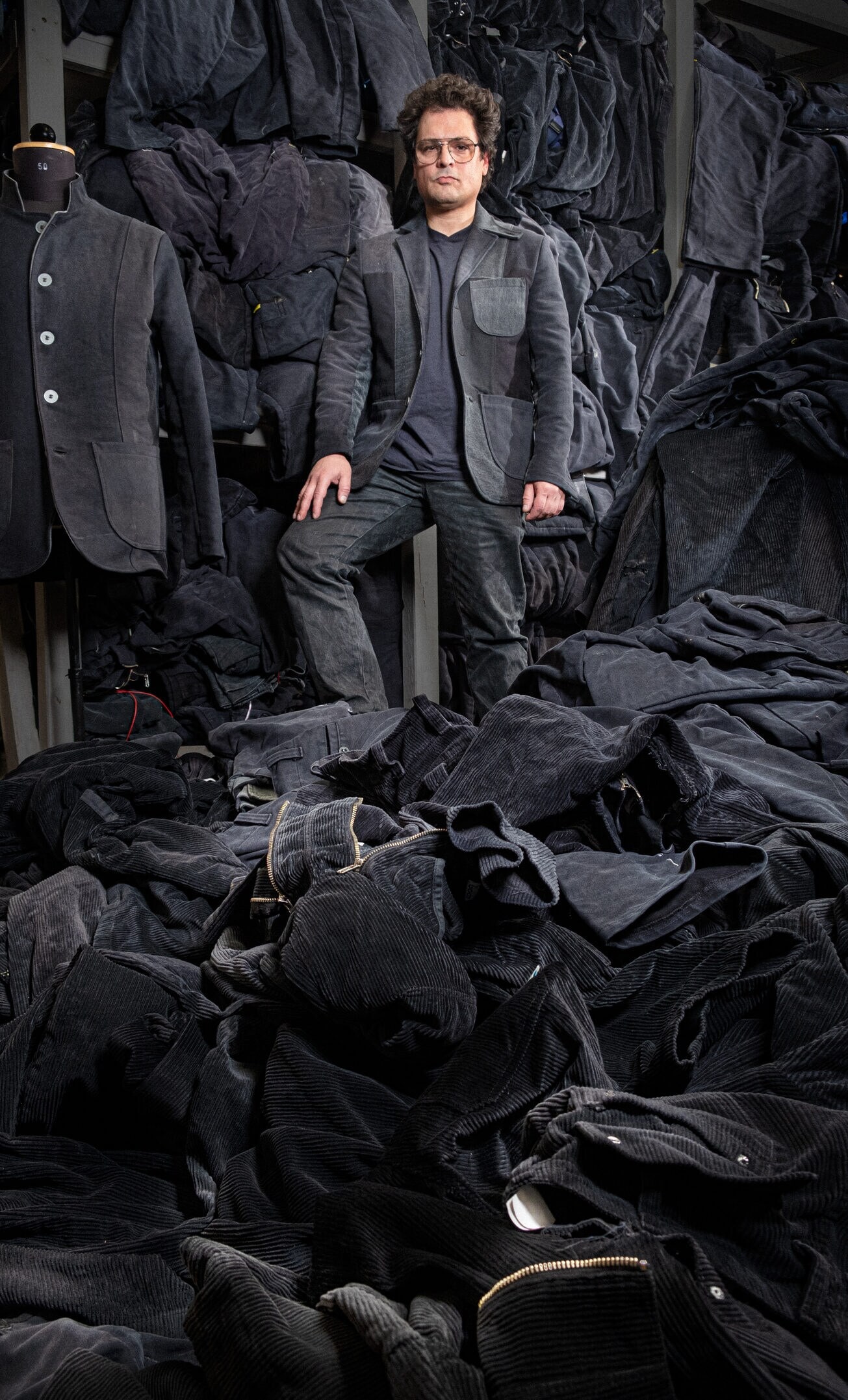 Ein Mann in Jeanskleidung steht inmitten von Haufen weiterer Jeanskleidung. Ein Mann in Jeanskleidung steht inmitten von Haufen weiterer Jeanskleidung.