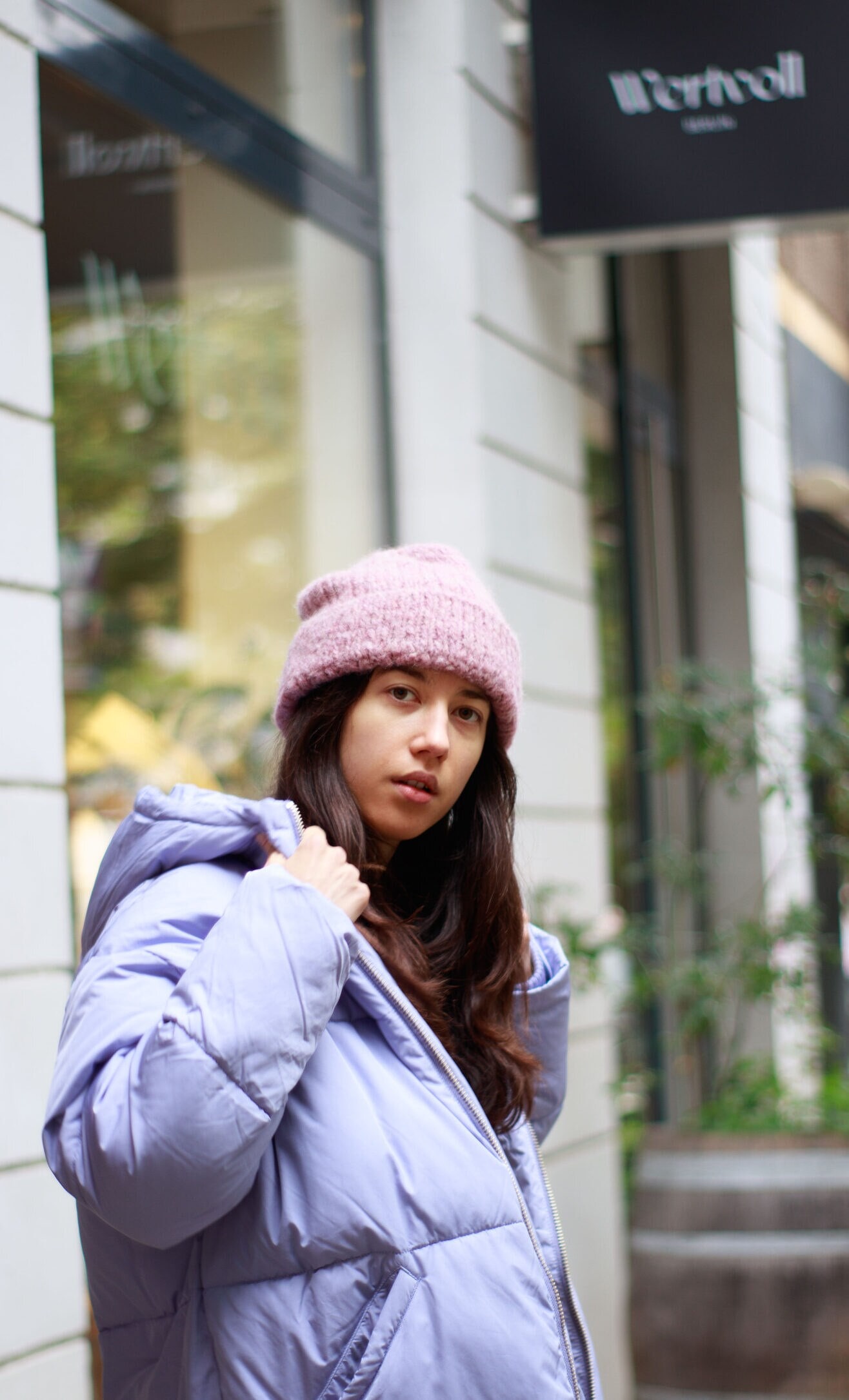 Eine Frau in lilafarbener Jacke und rosa Mütze vor einem Geschäft. Eine Frau in lilafarbener Jacke und rosa Mütze vor einem Geschäft.