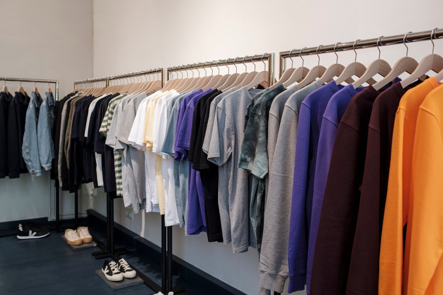 Mehrere Kleiderständer mit Kleidung, darunter stehen Schuhe.