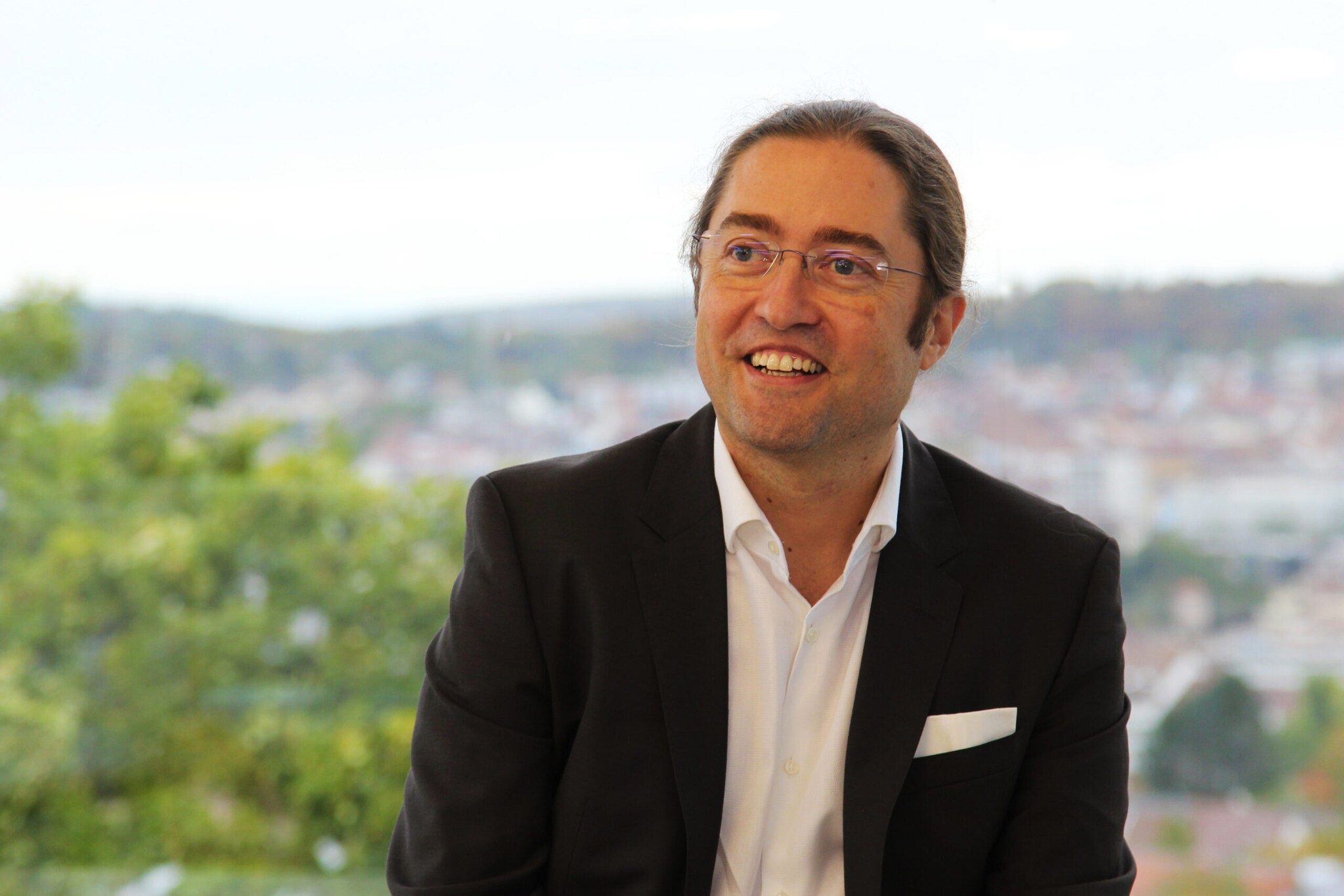 Ein Mann mit Pferdeschwanz und Brille in einem schwarzen Anzug