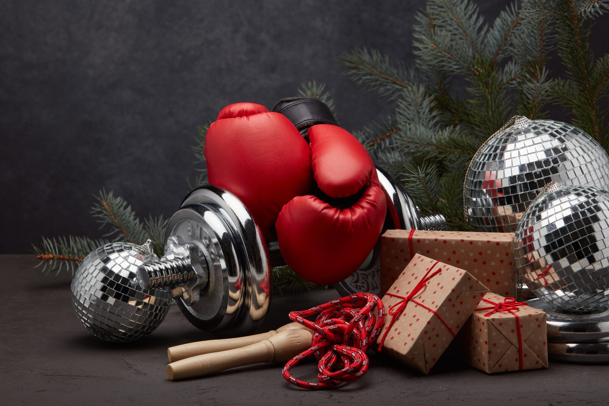 Stillleben mit roten Sportutensilien und Geschenken mit Tannenzweig vor dunklem Hintergrund