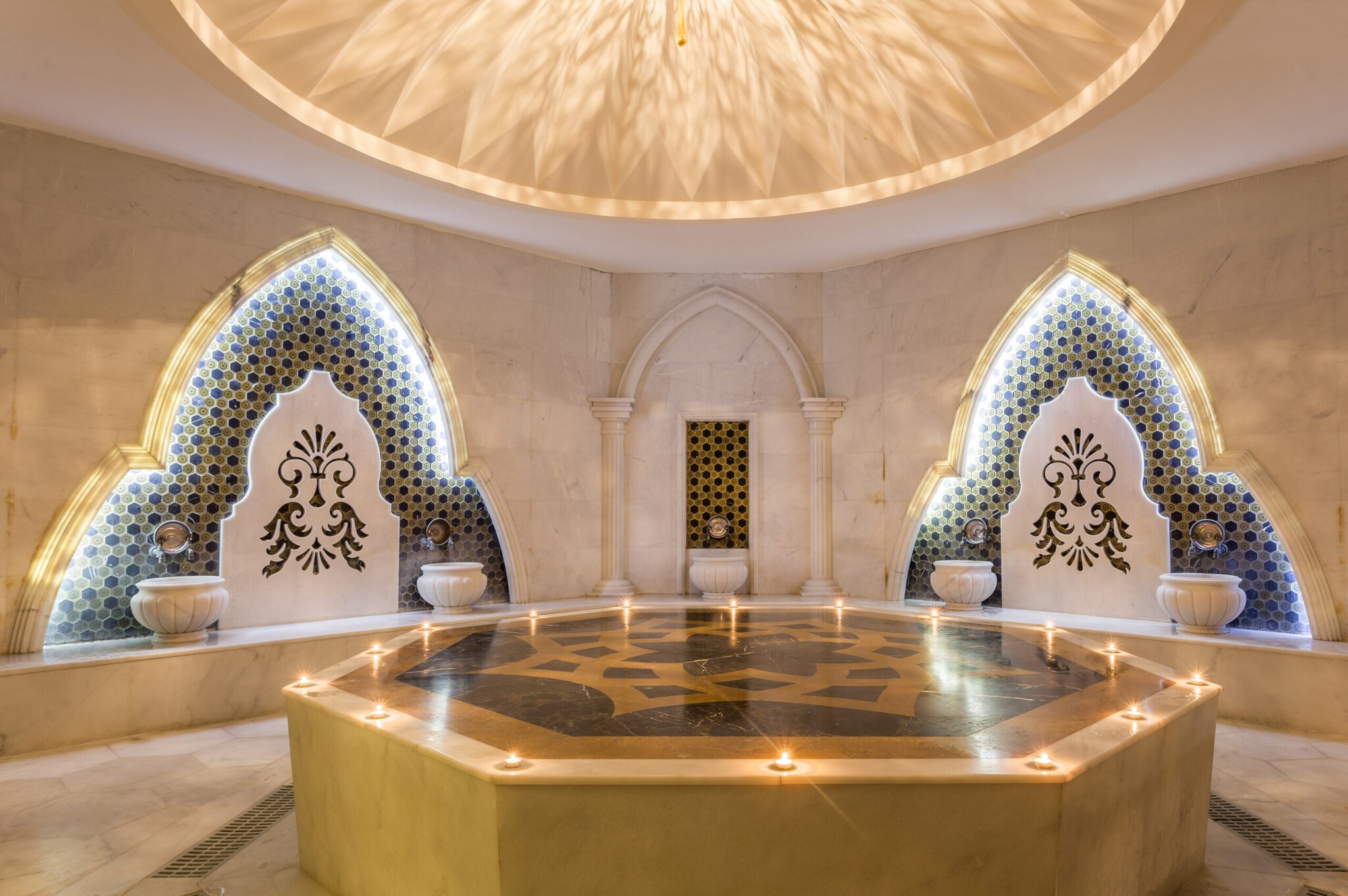 Elegantes, orientalischs Hamam mit goldfarbenem Nabelstein im Zentrum, darauf brennende Kerzen