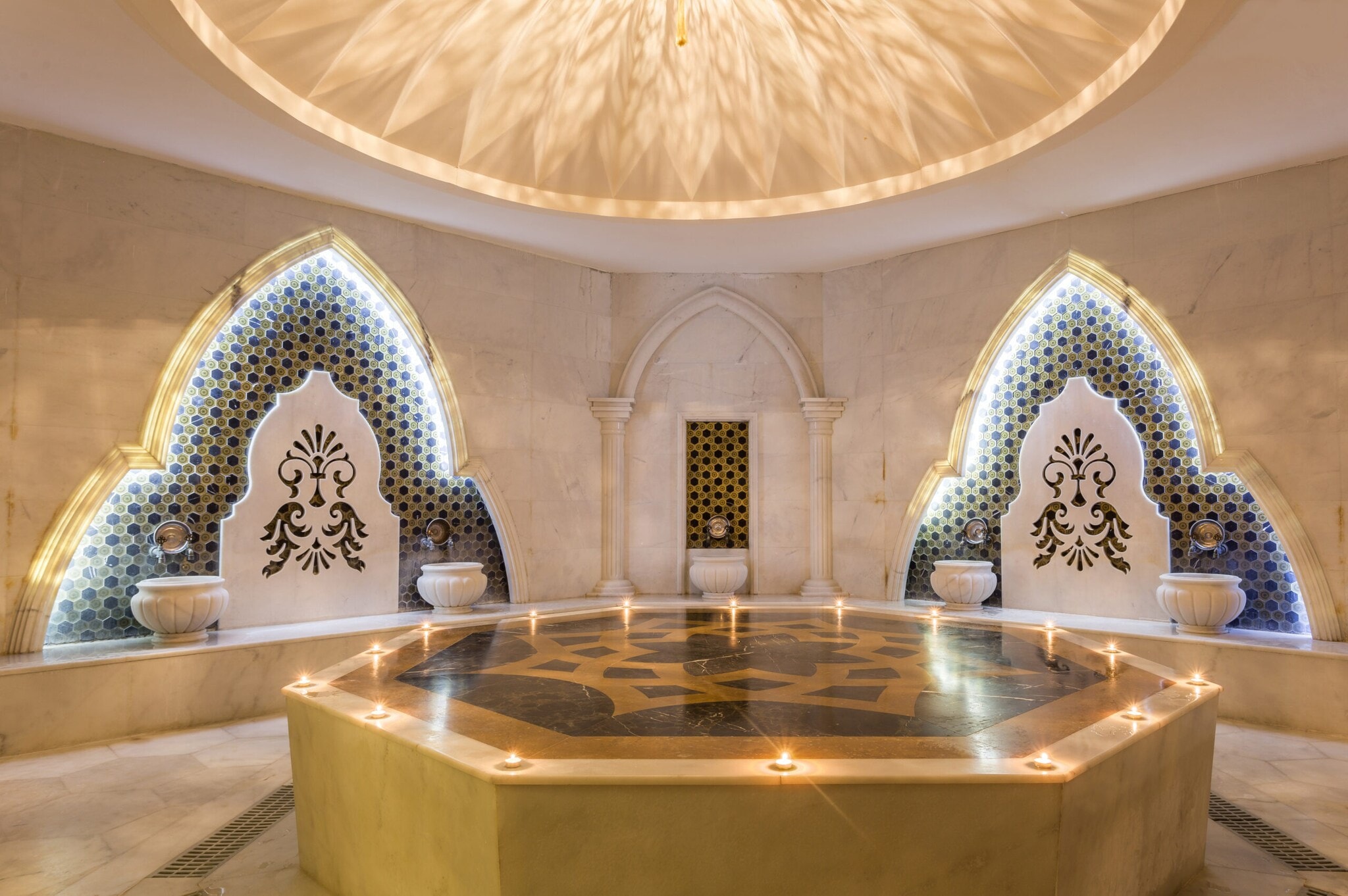 Elegantes, orientalischs Hamam mit goldfarbenem Nabelstein im Zentrum, darauf brennende Kerzen Elegantes, orientalischs Hamam mit goldfarbenem Nabelstein im Zentrum, darauf brennende Kerzen