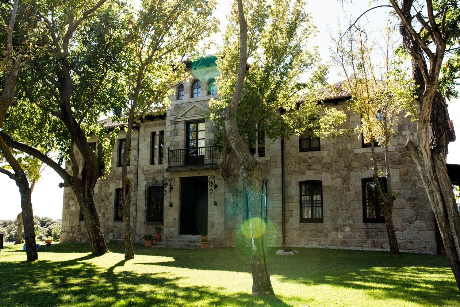 Fassade eines herrschaftlichen Landguts im mediterranen Stil, davor eine Rasenfläche mit Bäumen