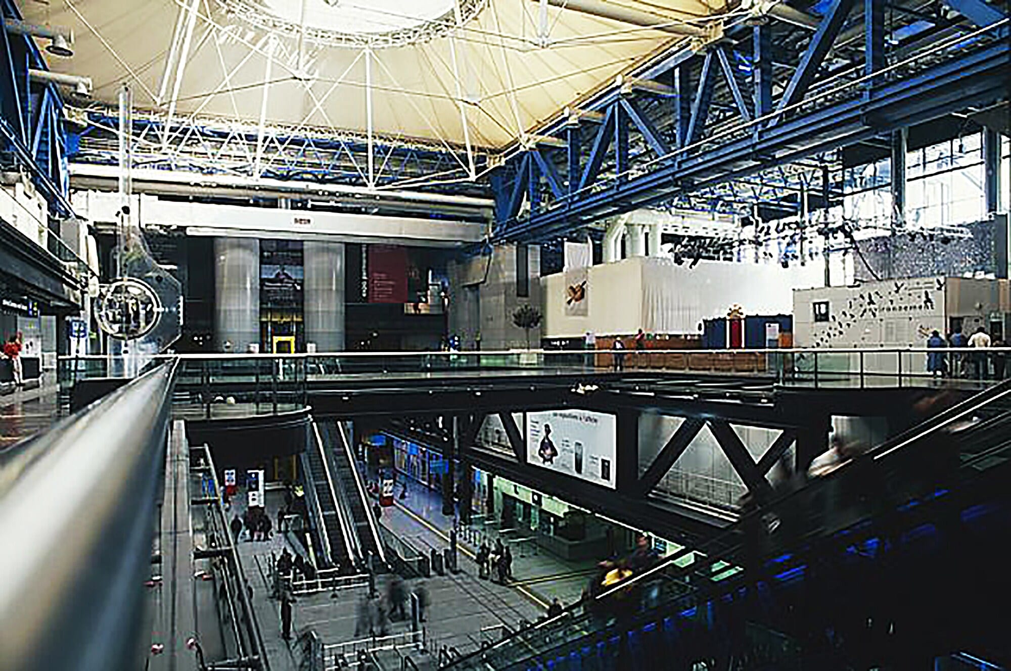 Innenaufnahme einer belebten Eingangshalle eines modernen, industriellen Gebäudes auf zwei Ebenen, die mit Rolltreppen verbunden sind Innenaufnahme einer belebten Eingangshalle eines modernen, industriellen Gebäudes auf zwei Ebenen, die mit Rolltreppen verbunden sind