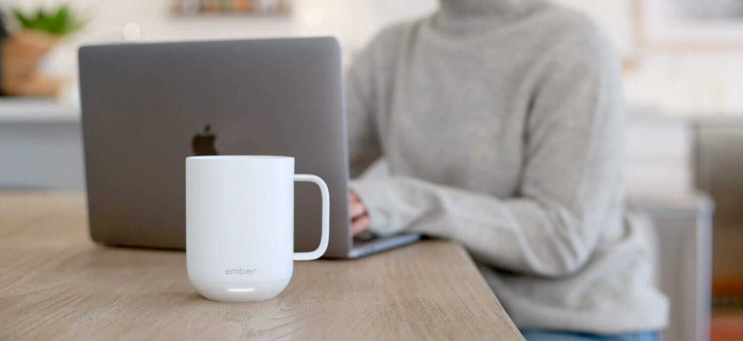 Eine weiße Keramiktasse steht vor einem Laptop