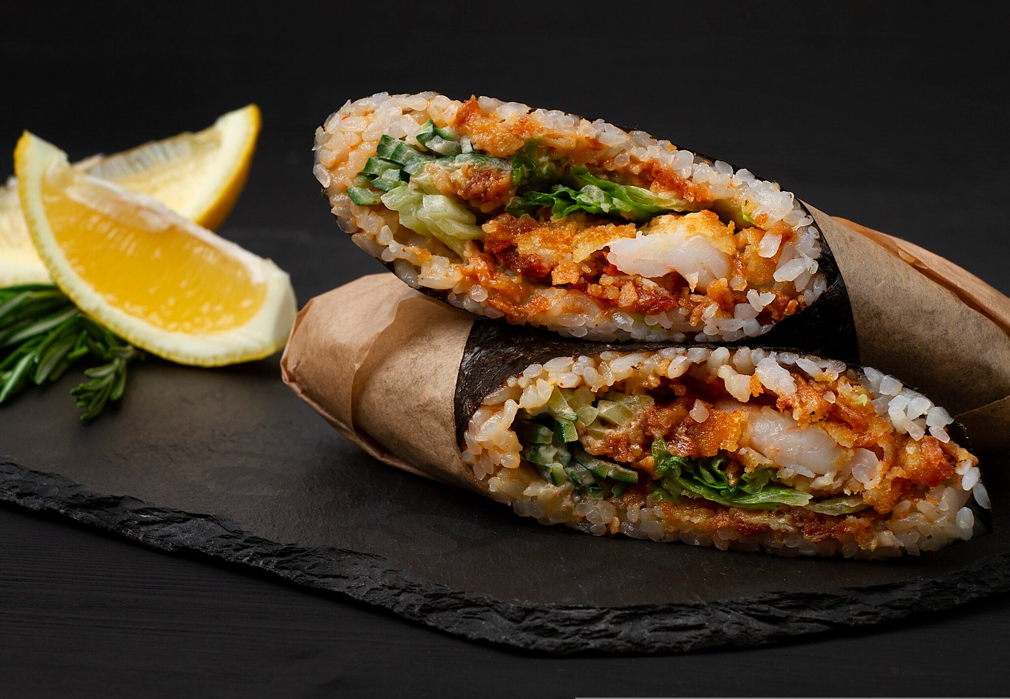 Zwei große Reisrollen mit Gemüse und Garnele auf schwarzer Schieferplatte angerichtet