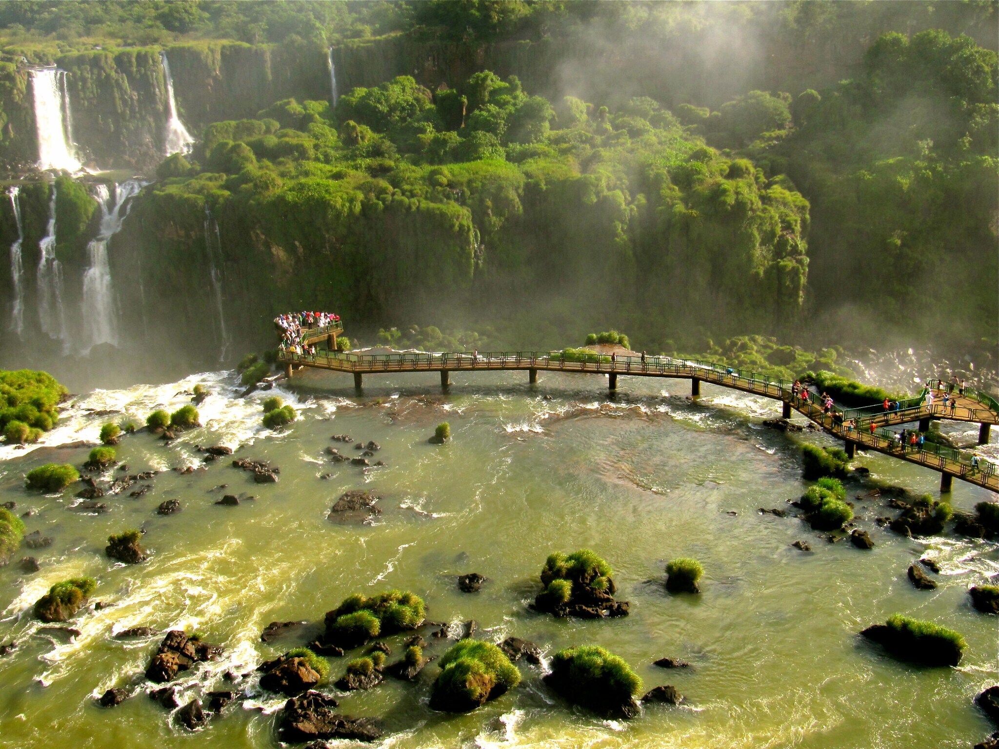 Panorama eines Naturparks mit Wasserfällen und Regenwald, in dem Besucher auf einem auf Stelzen gebauten Weg über das Wasser laufen