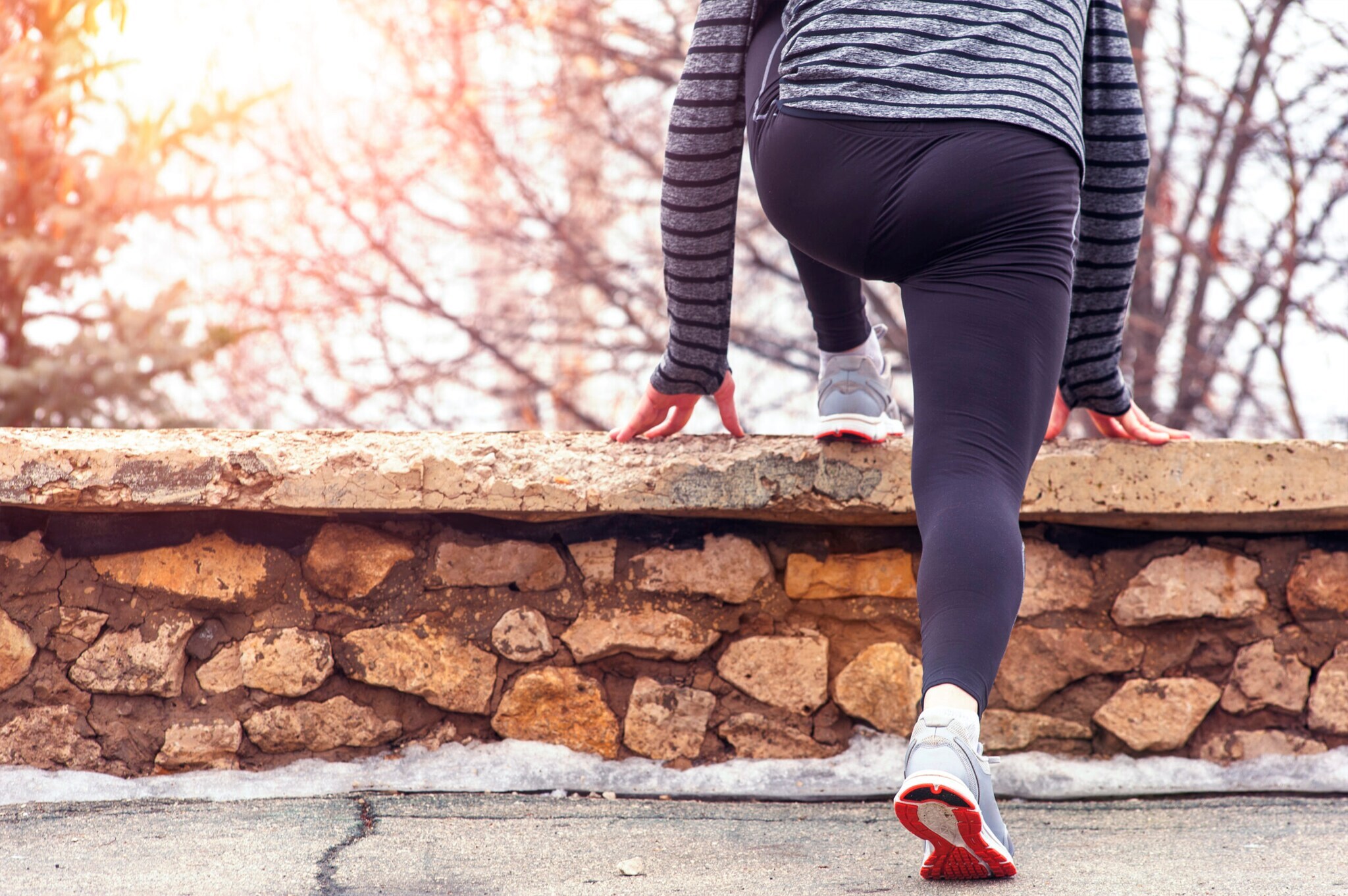 Jogger:in von hinten beim Dehnen der Wade an einem Mäuerchen