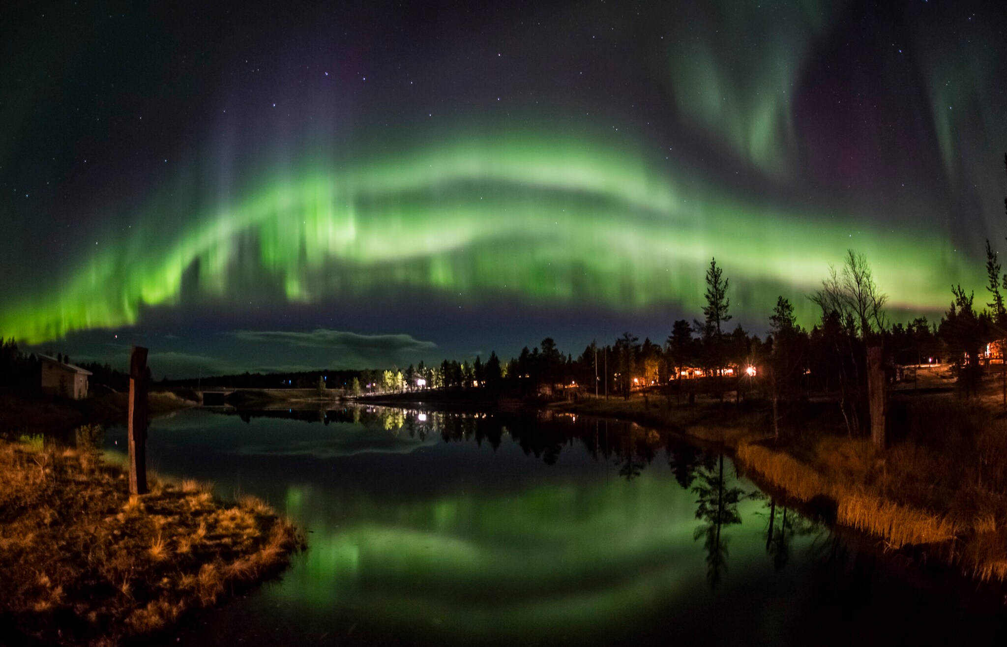 Grünes Polarlicht über Landschaftspanorama mit spiegelndem Wasser und einGrünes Polarlicht über Landschaftspanorama mit spiegelndem Wasser und einem beleuchteten Haus bei Nacht