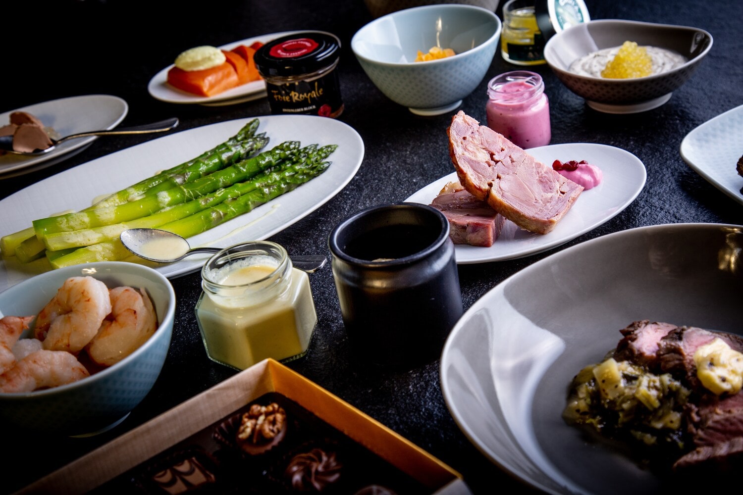 Nahaufnahme einer Auswahl an Delikatessen angerichtet auf verschiedenen Tellern auf schwarzem Untergrund Nahaufnahme einer Auswahl an Delikatessen angerichtet auf verschiedenen Tellern auf schwarzem Untergrund