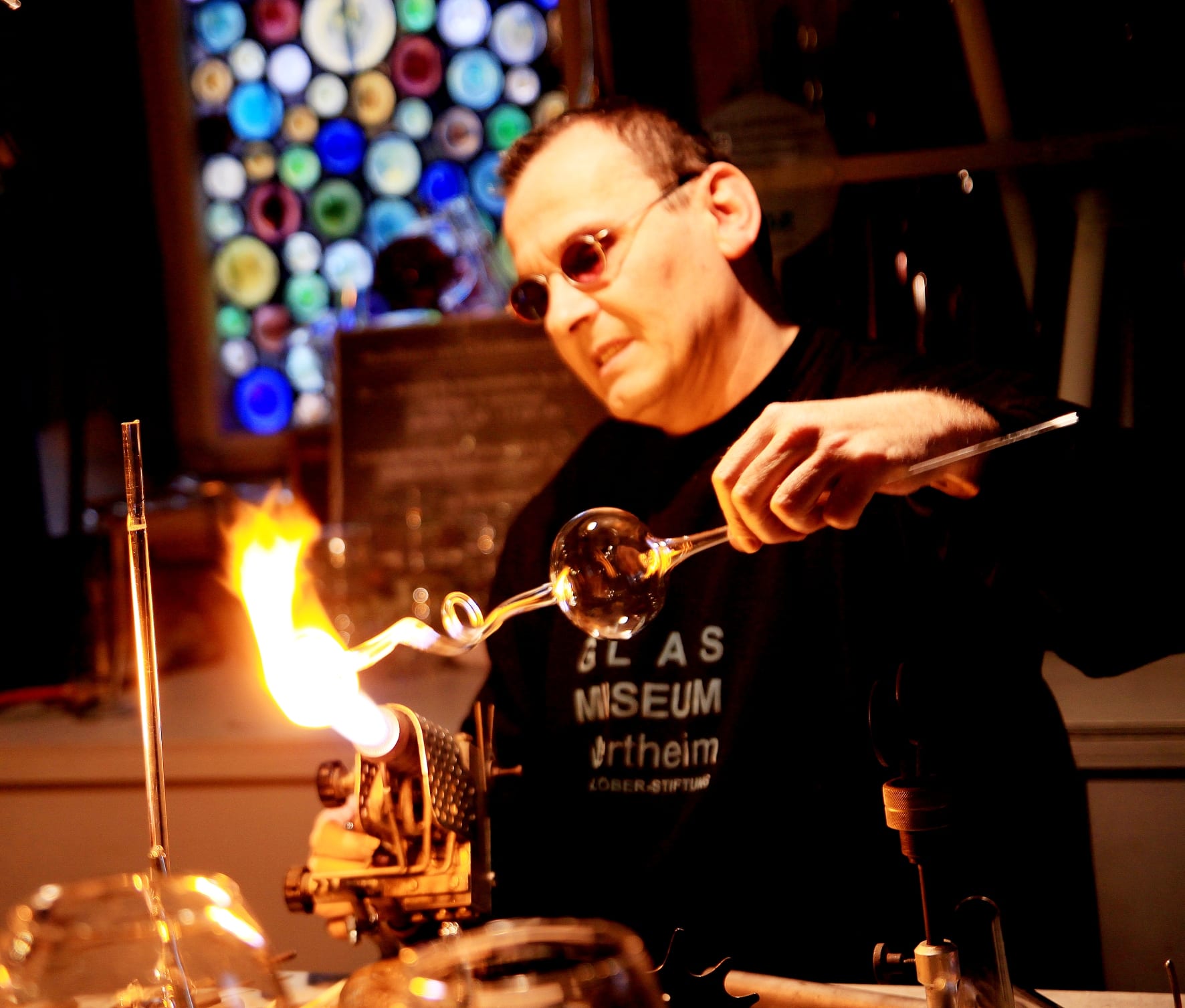 Ein Mann hält ein geblasenes Glasstück in eine Flamme