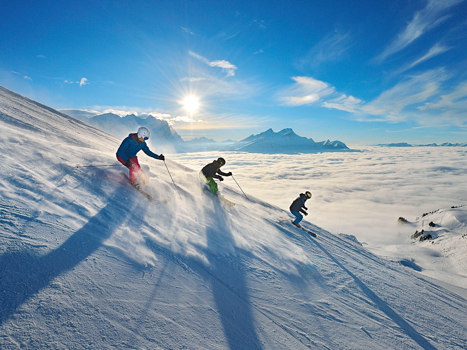 Drei Skifahrer:innen bei der Abfahrt im freien Gelände