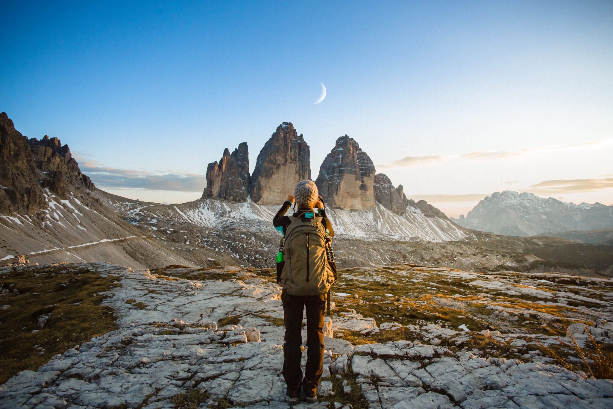 Ein Wanderer fotografiert eine Landschaft mit Mond bei Tageslicht.