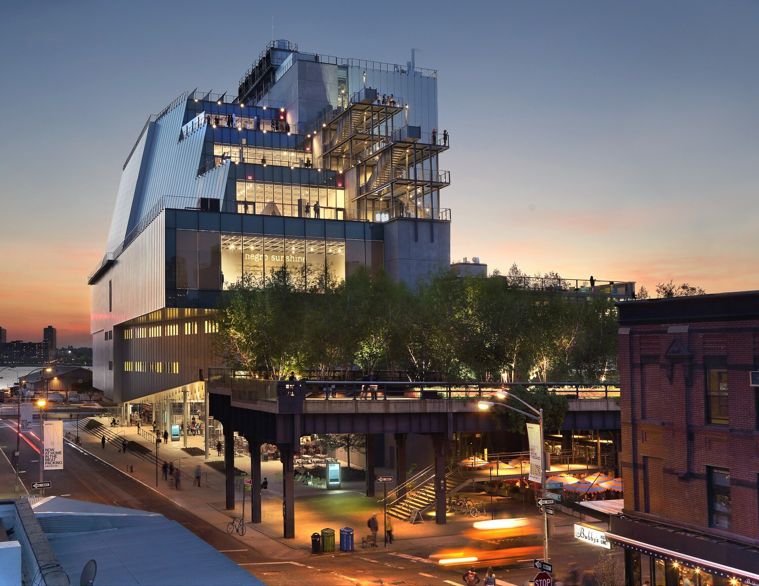 Beleuchteter, moderner Gebäudekomplex des Whitney Museum of Art mit Besuchern auf unterschiedlichen Terrassen in der Abenddämmerung Beleuchteter, moderner Gebäudekomplex des Whitney Museum of Art mit Besuchern auf unterschiedlichen Terrassen in der Abenddämmerung