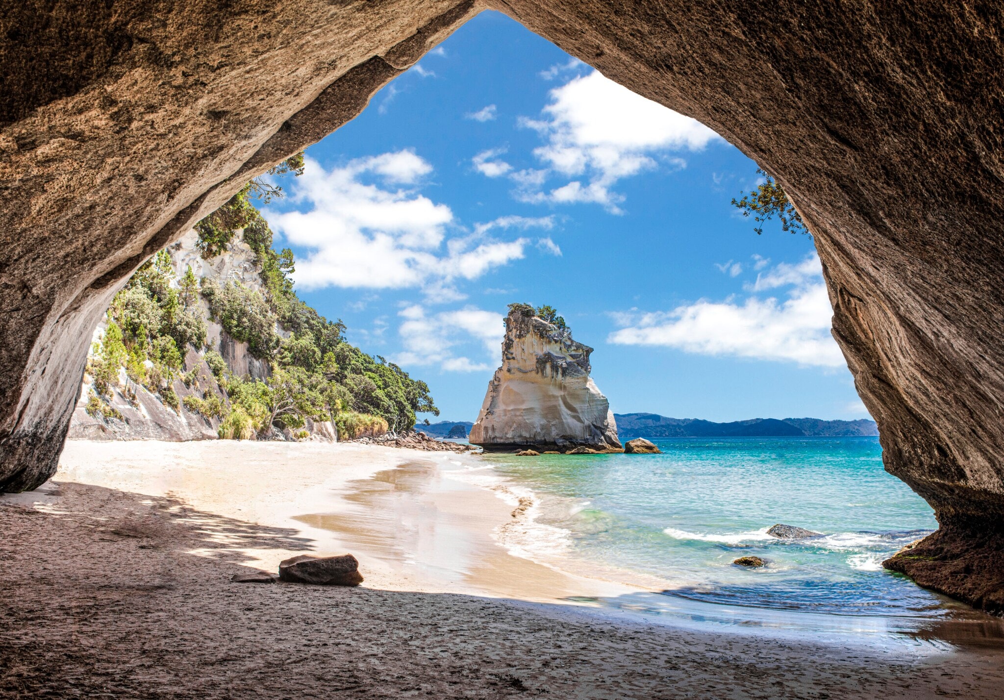 Im Vordergrund ein Felsbrocken, dahinter ein Sandstrand, umringt von Felsen und türkisfarbenem Meer Im Vordergrund ein Felsbrocken, dahinter ein Sandstrand, umringt von Felsen und türkisfarbenem Meer