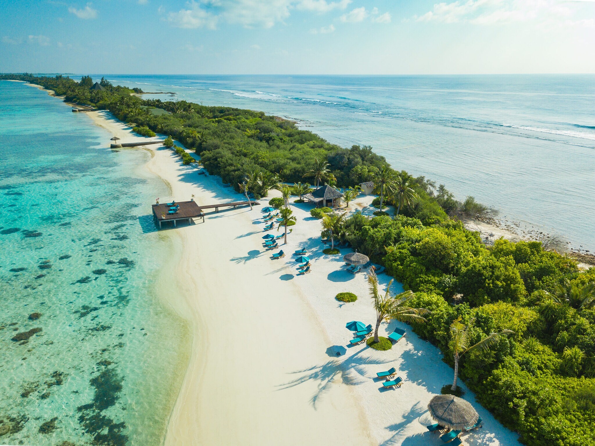 Aufsicht einer Landzunge mit weißem Sandstrand und grüner Vegetation im türkisblauen Meer, vereinzelt blaue Liegen am Strand Aufsicht einer Landzunge mit weißem Sandstrand und grüner Vegetation im türkisblauen Meer, vereinzelt blaue Liegen am Strand