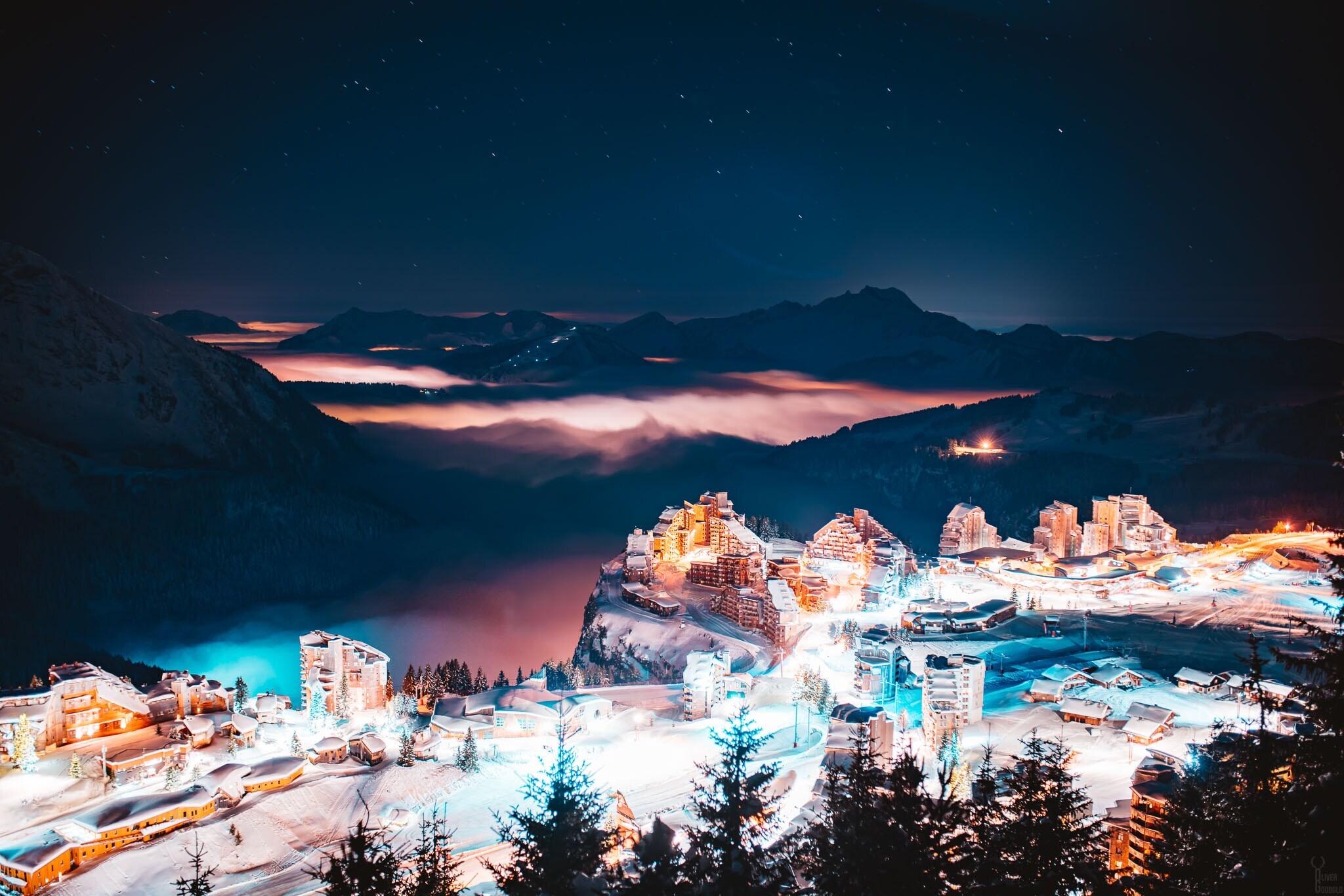 Eine erleuchtete Stadt bei Nacht, im Hintergrund dunkle Berge.