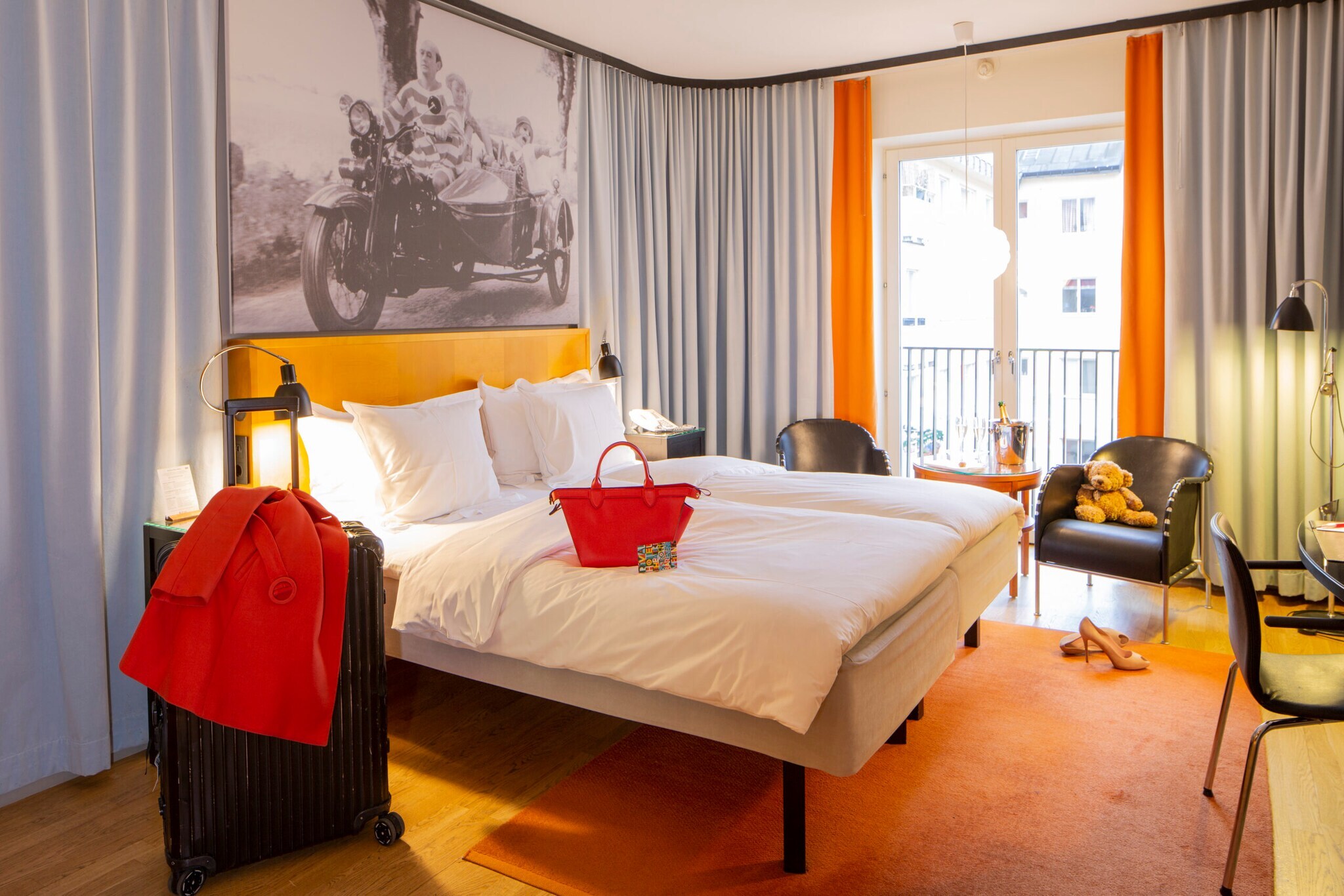Hotelzimmer. Im Mittelpunkt ein Bett, daneben Koffer, Stühle, Vorhänge