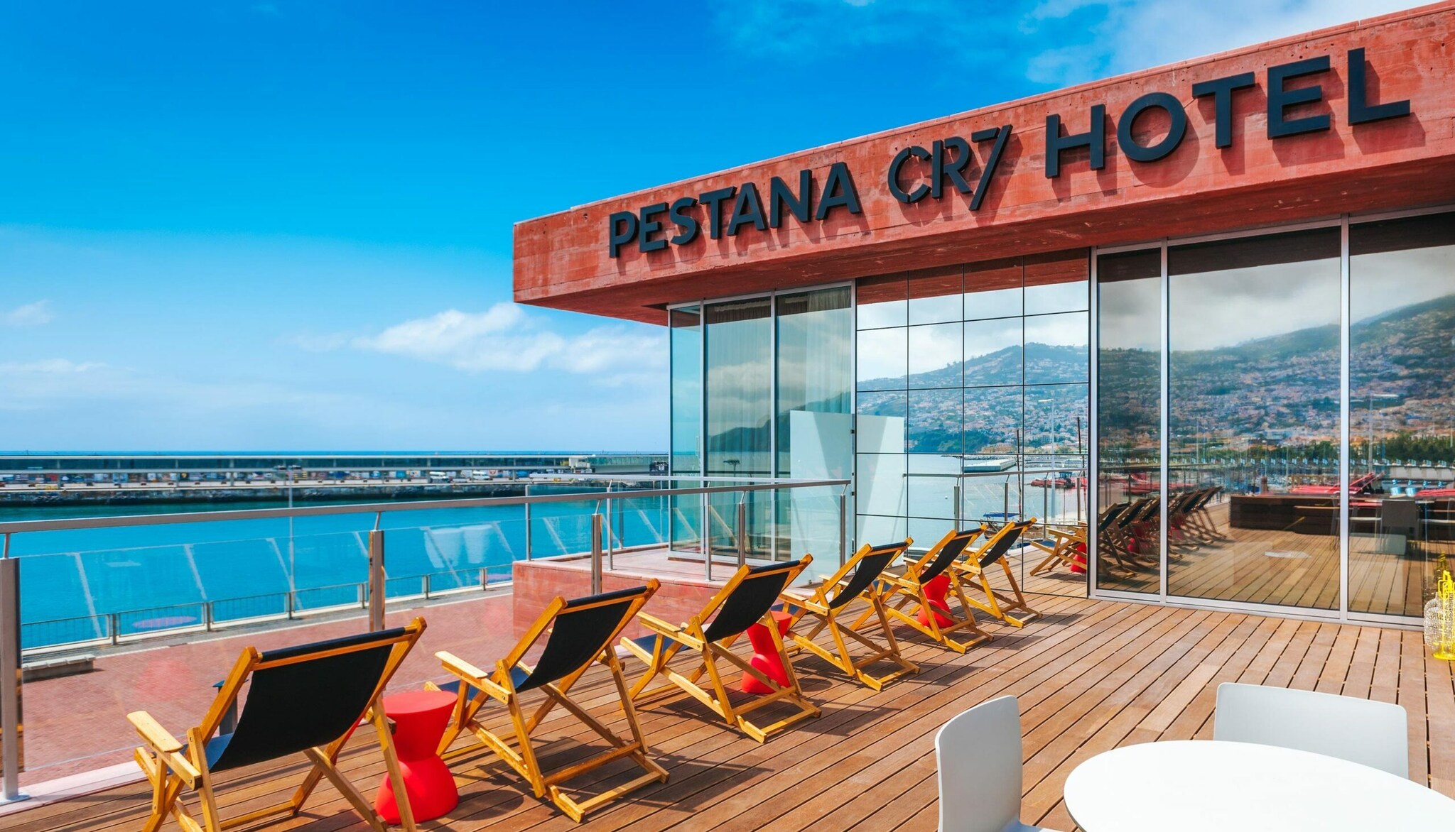 Terrasse mit Sonnenstühlen, im Hintergrund Wasser und Berge Terrasse mit Sonnenstühlen, im Hintergrund Wasser und Berge