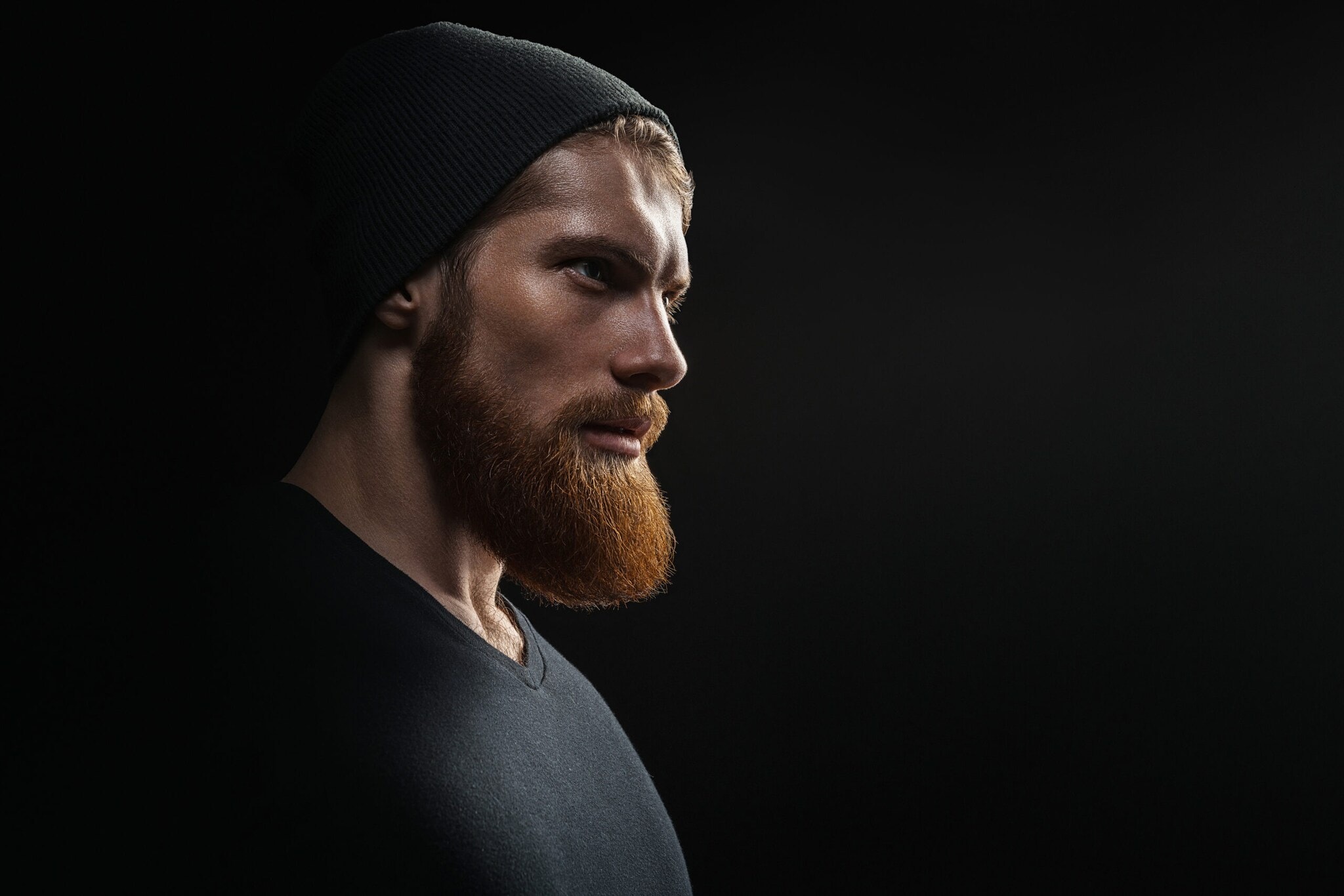Porträt eines Mannes mit Vollbart und schwarzer Kleidung und Mütze vor schwarzem Hintergrund